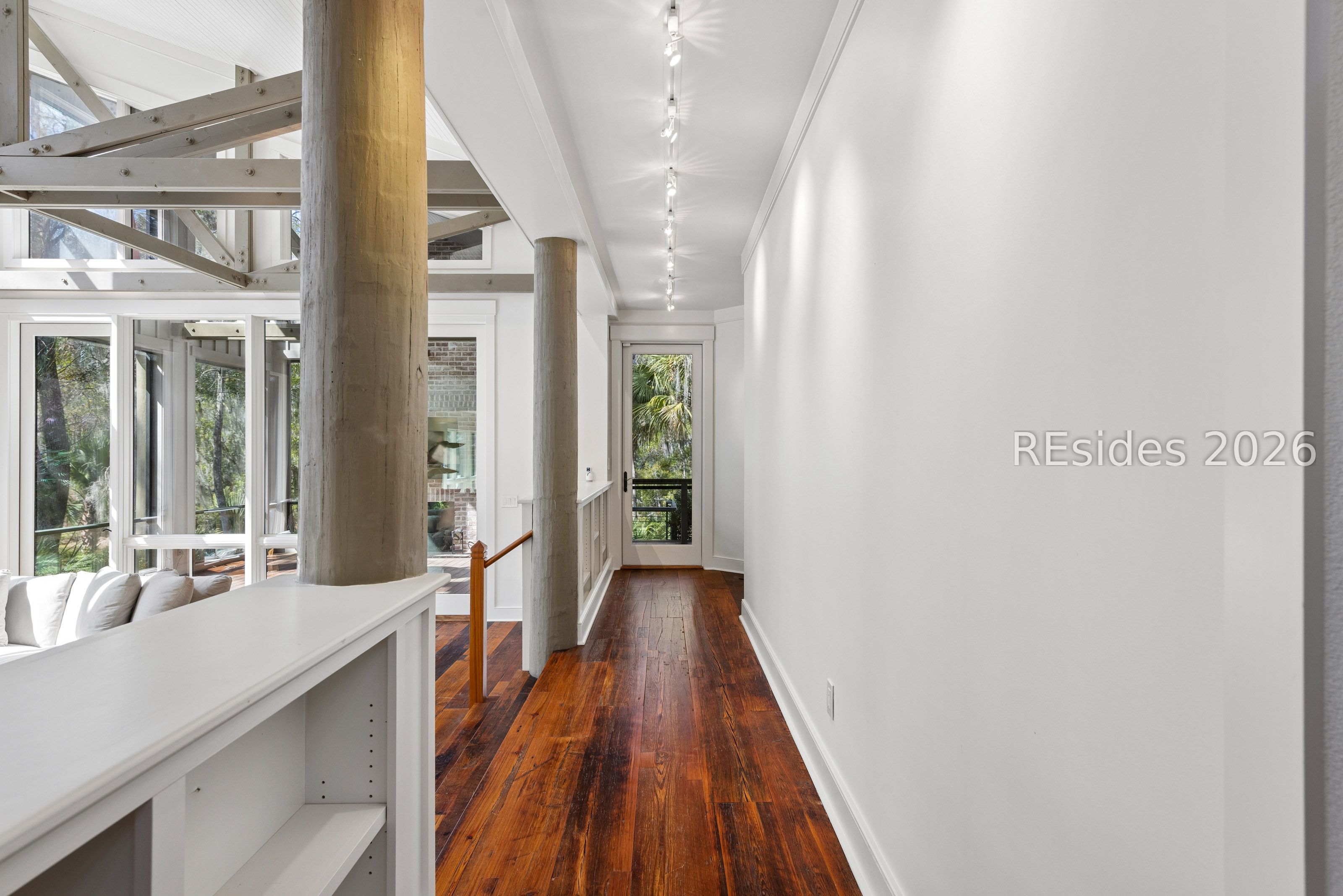 Bright hallway with warm hardwood floors, exposed concrete columns and beams, and large windows.