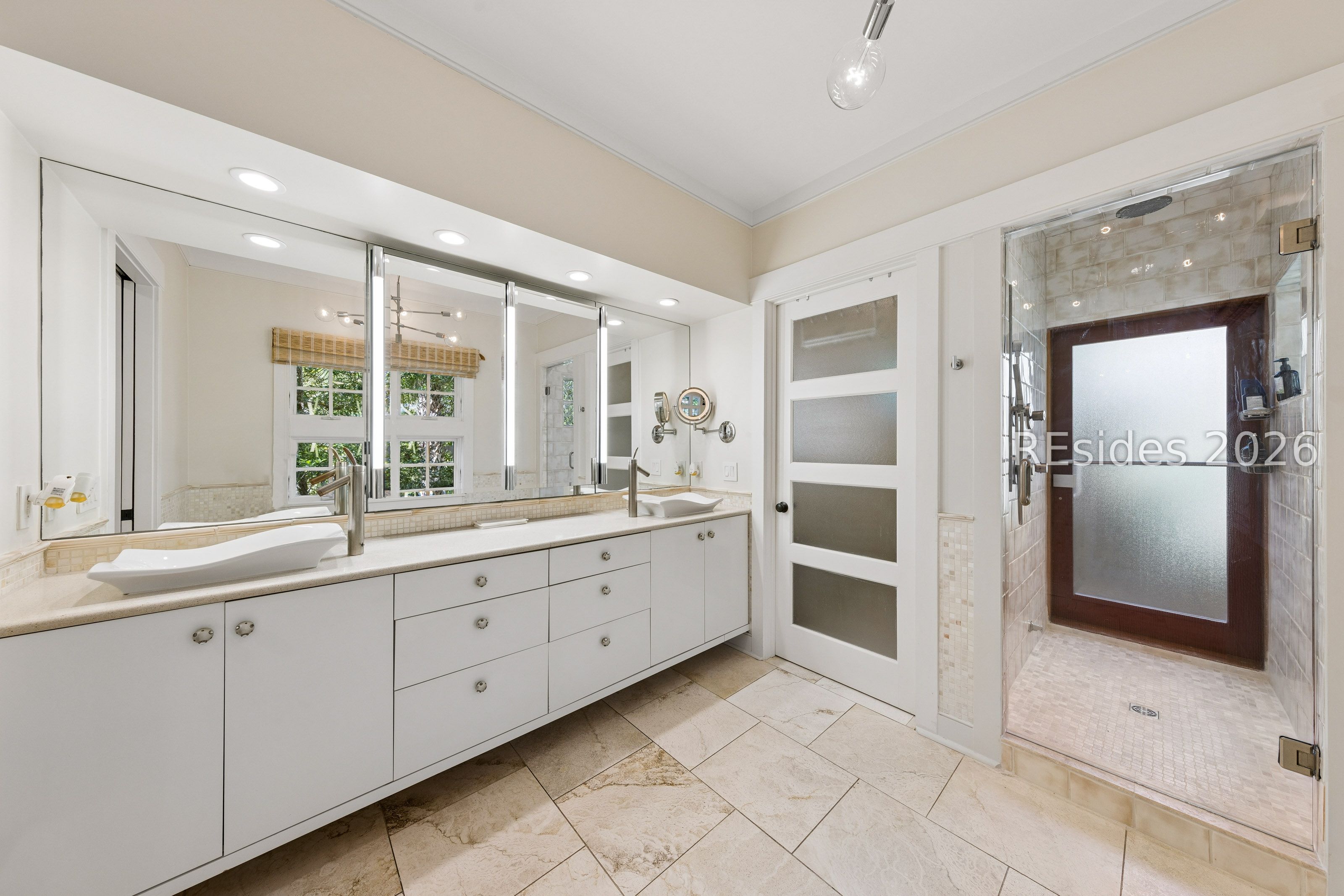 Bathroom with a long white vanity and glass-enclosed tiled shower with a dark-framed door.