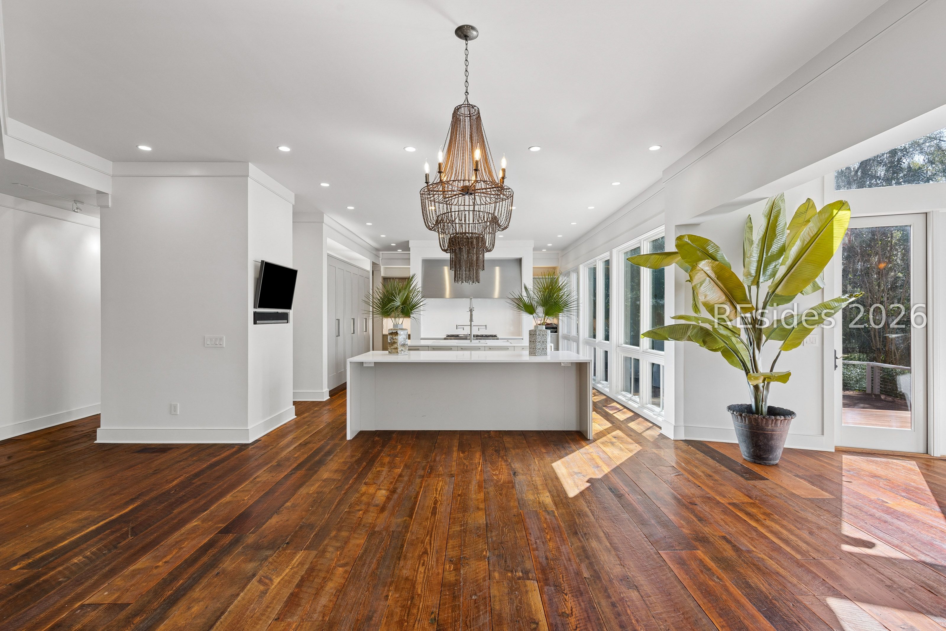 Bright kitchen with a white island, tiered chandelier, dark wood floors, and tall windows.