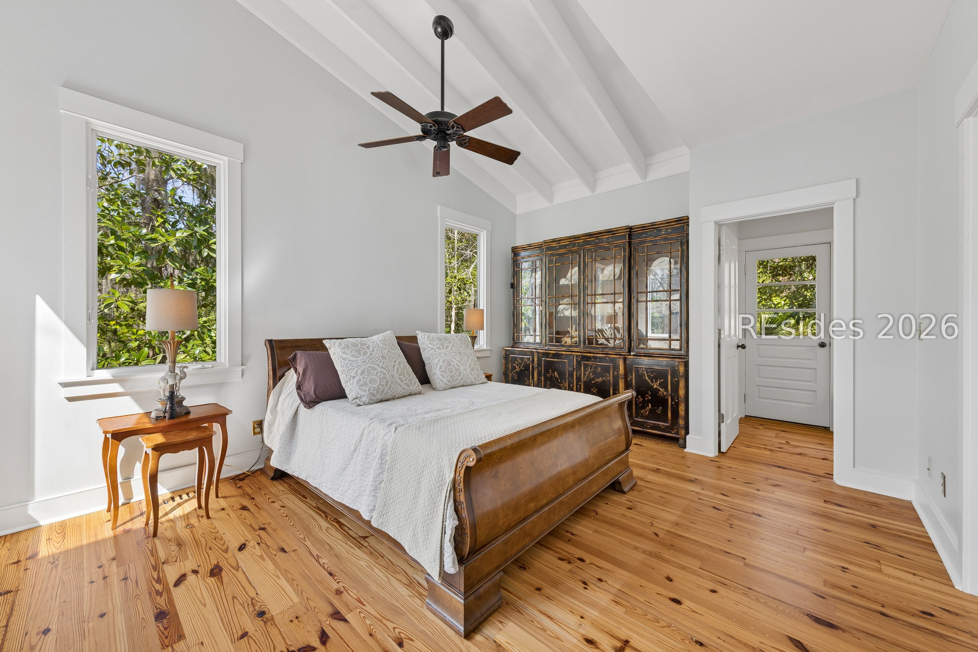 Bright bedroom with a vaulted beamed ceiling, hardwood floors, and a carved wooden bed.