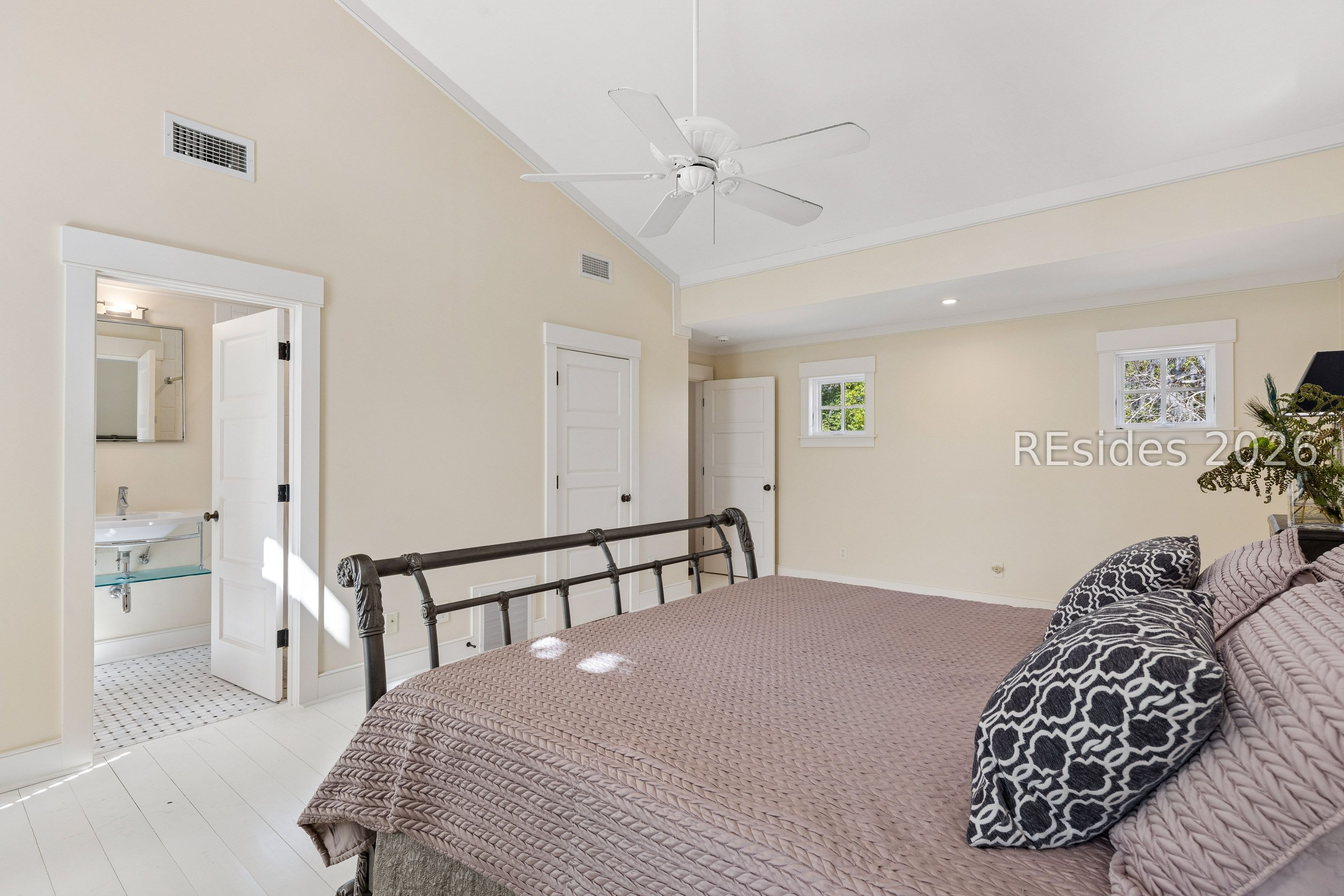 Bedroom with a vaulted ceiling, dark metal bed frame, mauve bedding, and an adjoining bathroom.