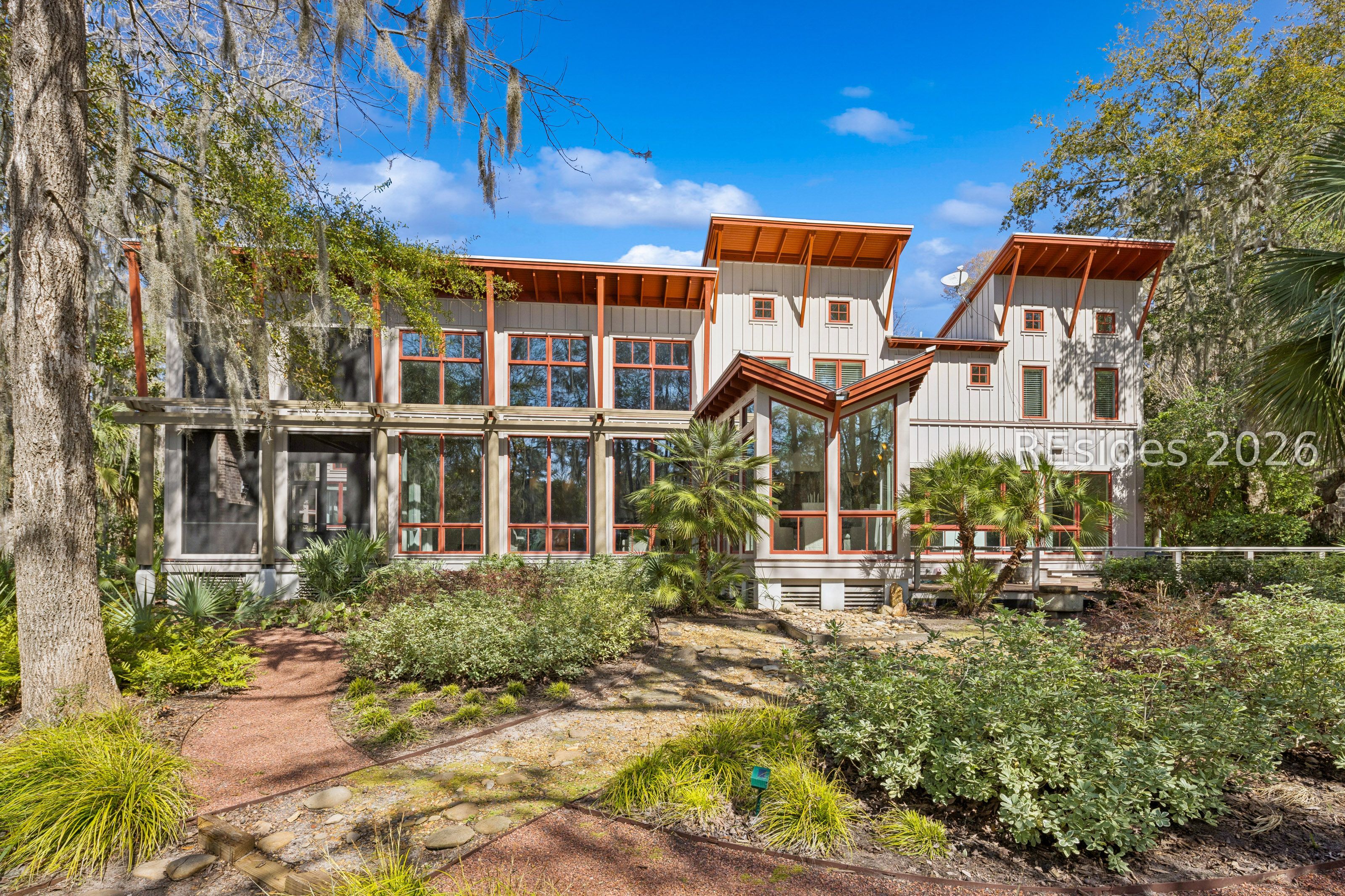 Contemporary gray-sided home with reddish-brown trim, large windows, and a landscaped garden path.
