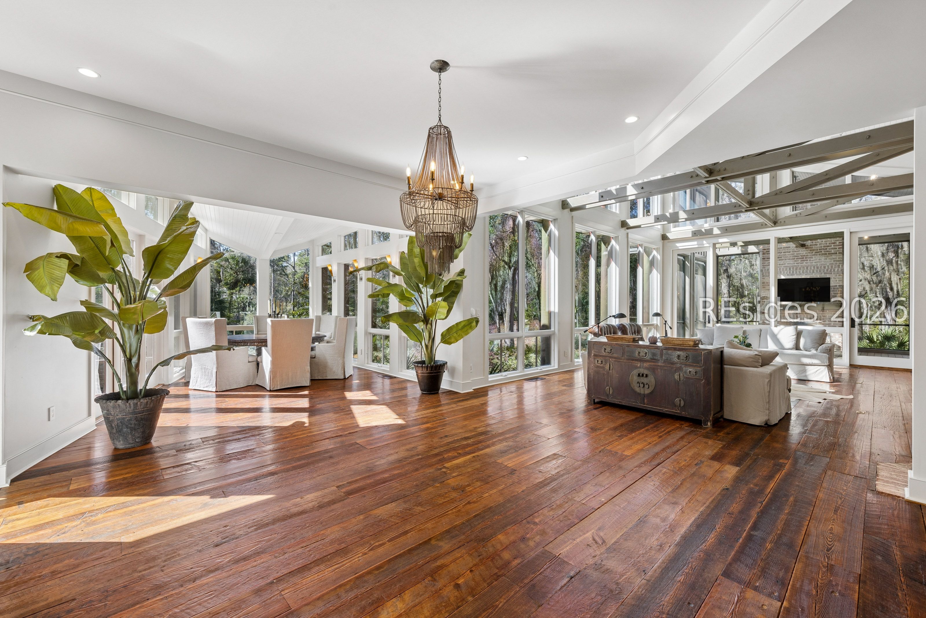 Open-plan living and dining room with exposed steel beams, wide-plank floors, and tall windows.