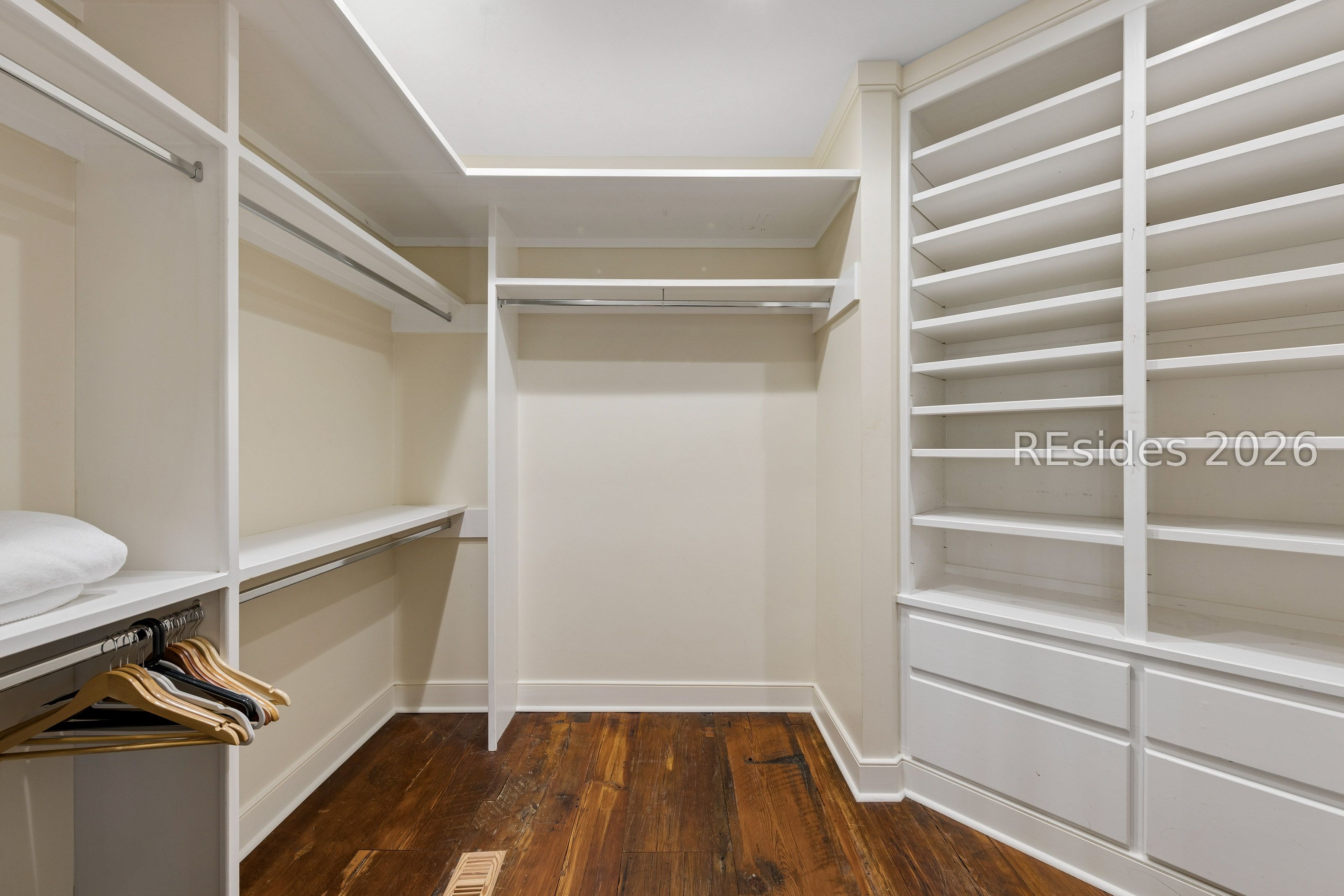 Walk-in closet with built-in shelving, drawers, hanging rails, and dark wood flooring.