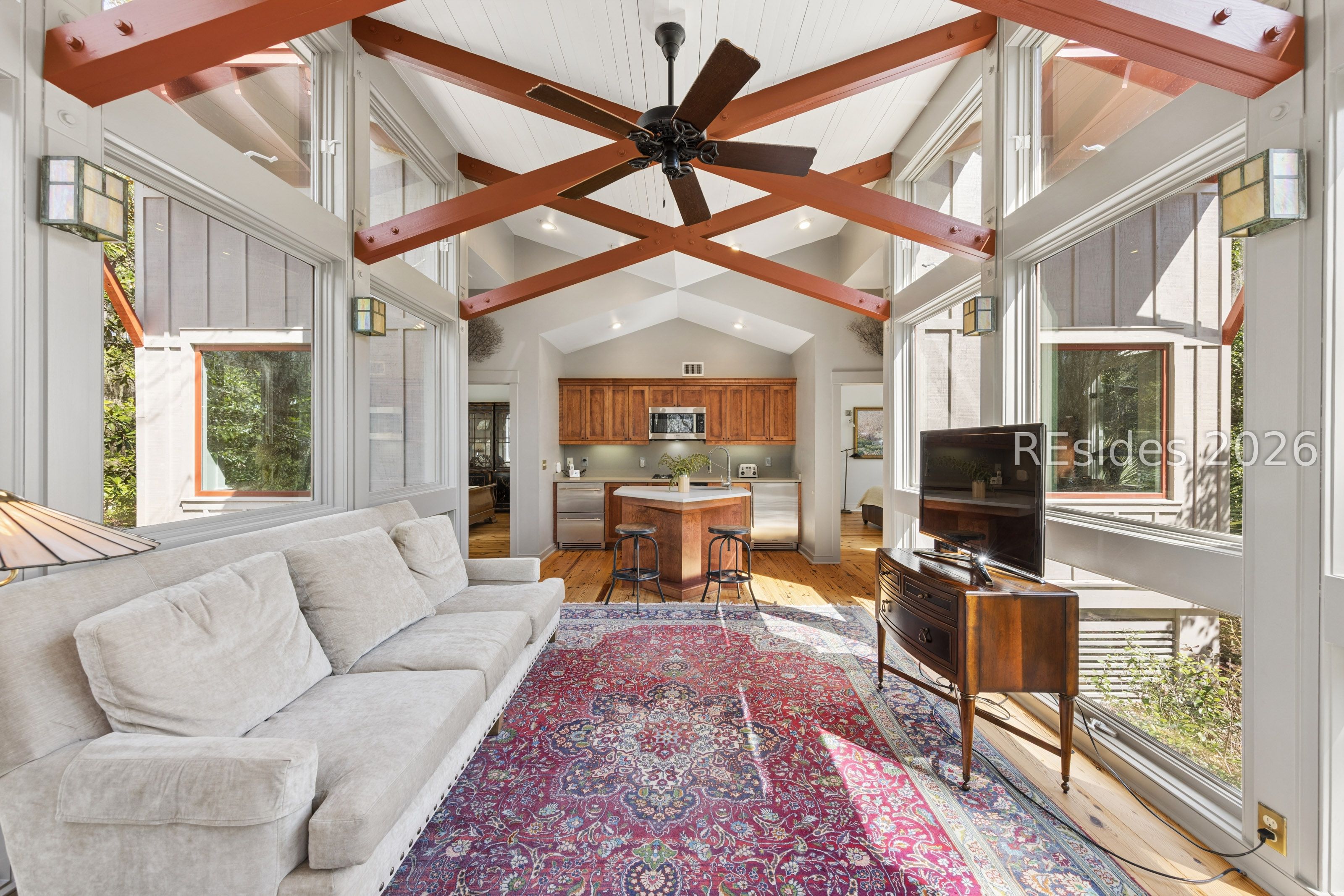 Living room with exposed wood beams, tall windows, a light sofa, and a patterned rug.