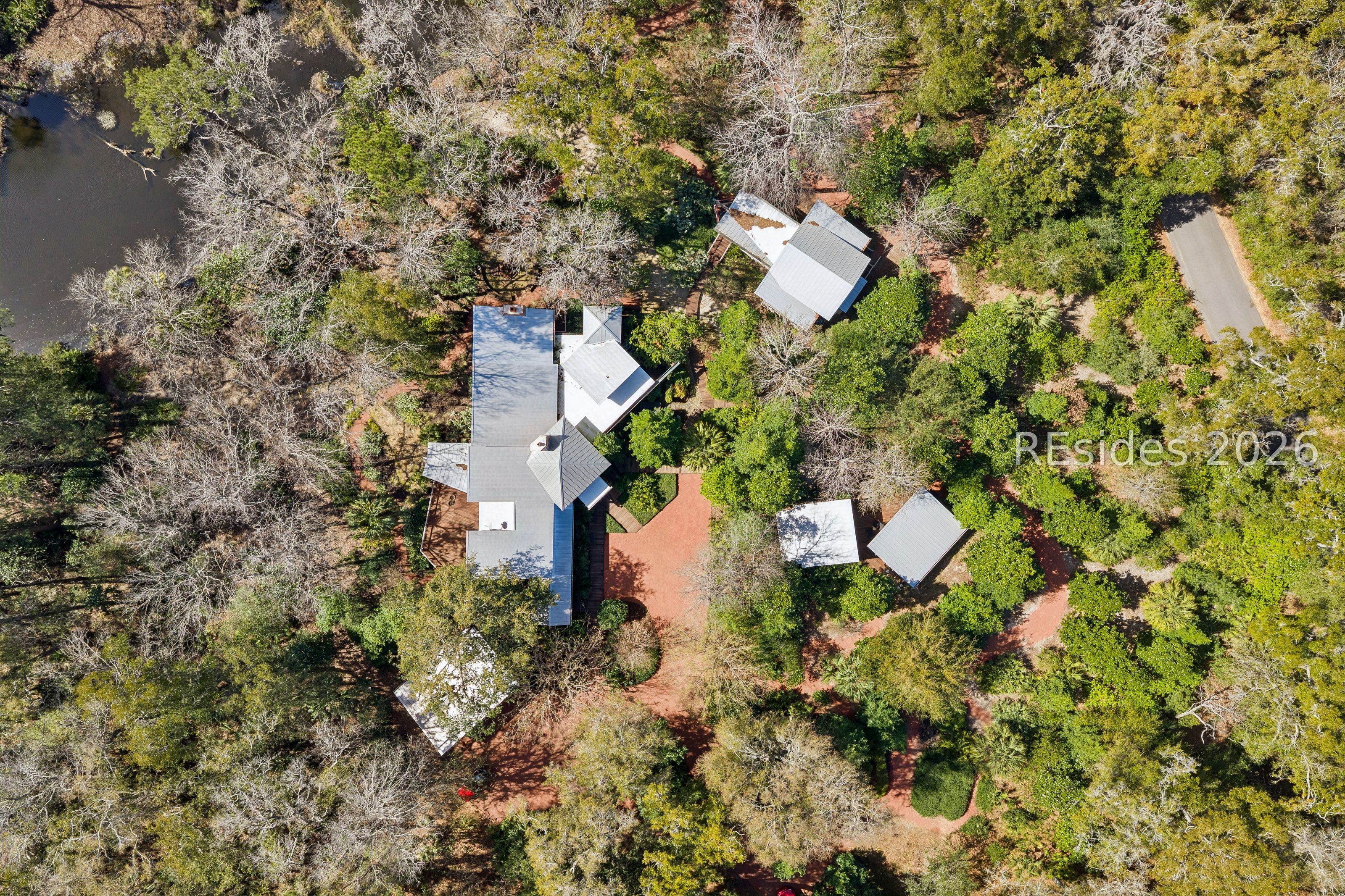 Aerial view of a wooded property with several buildings, red-earth paths, and water nearby.