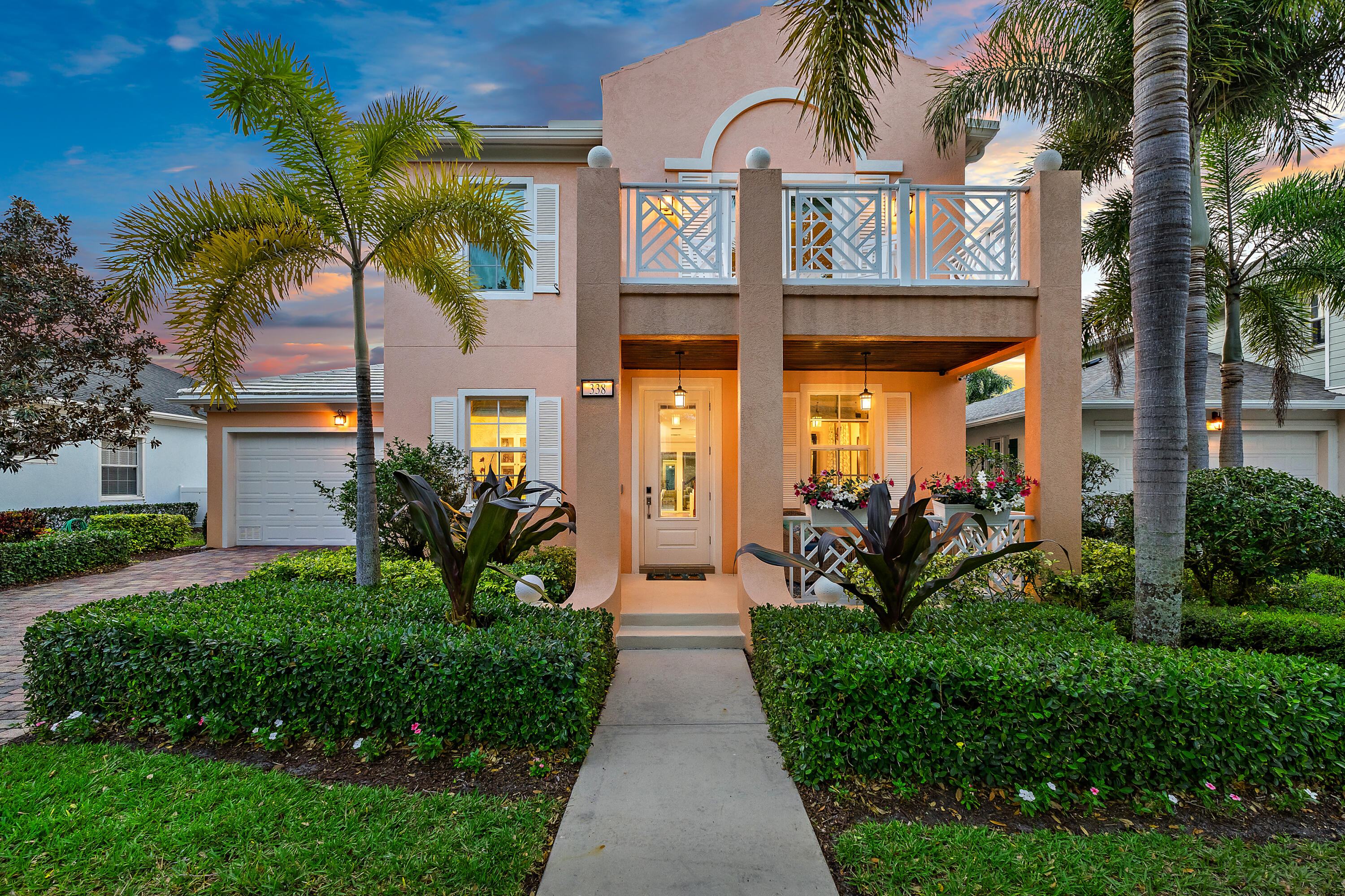 Two-story stucco home with a covered porch, geometric balcony railing, and palm landscaping at dusk.