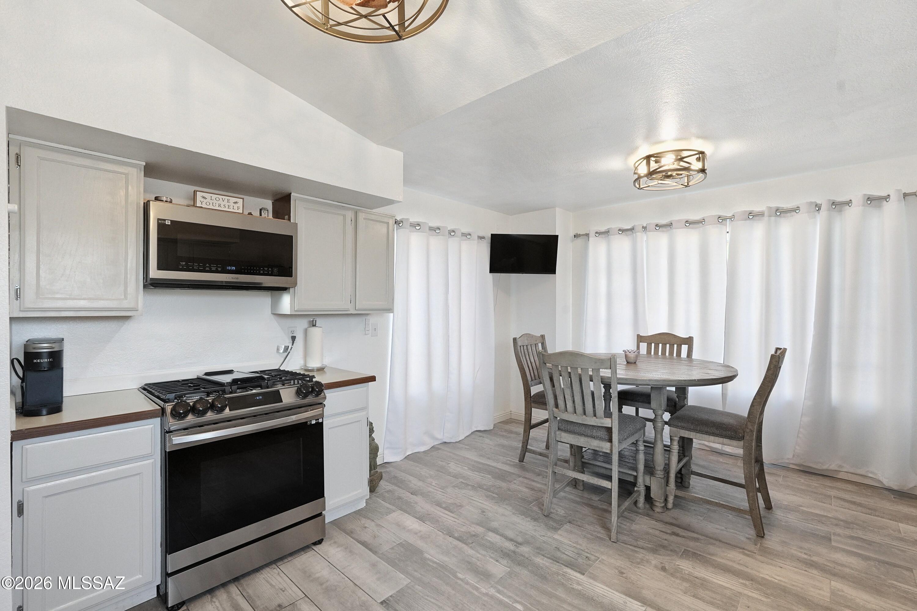 Kitchen and dining area with white cabinets, stainless steel appliances, and a round table beside curtained windows.