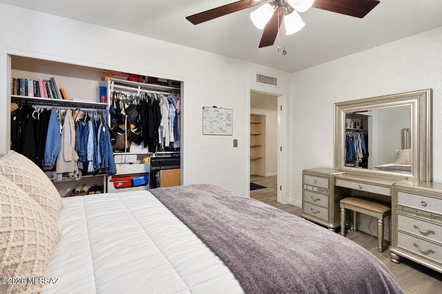 Bedroom with a large open clothes closet, silver vanity, and ceiling fan.