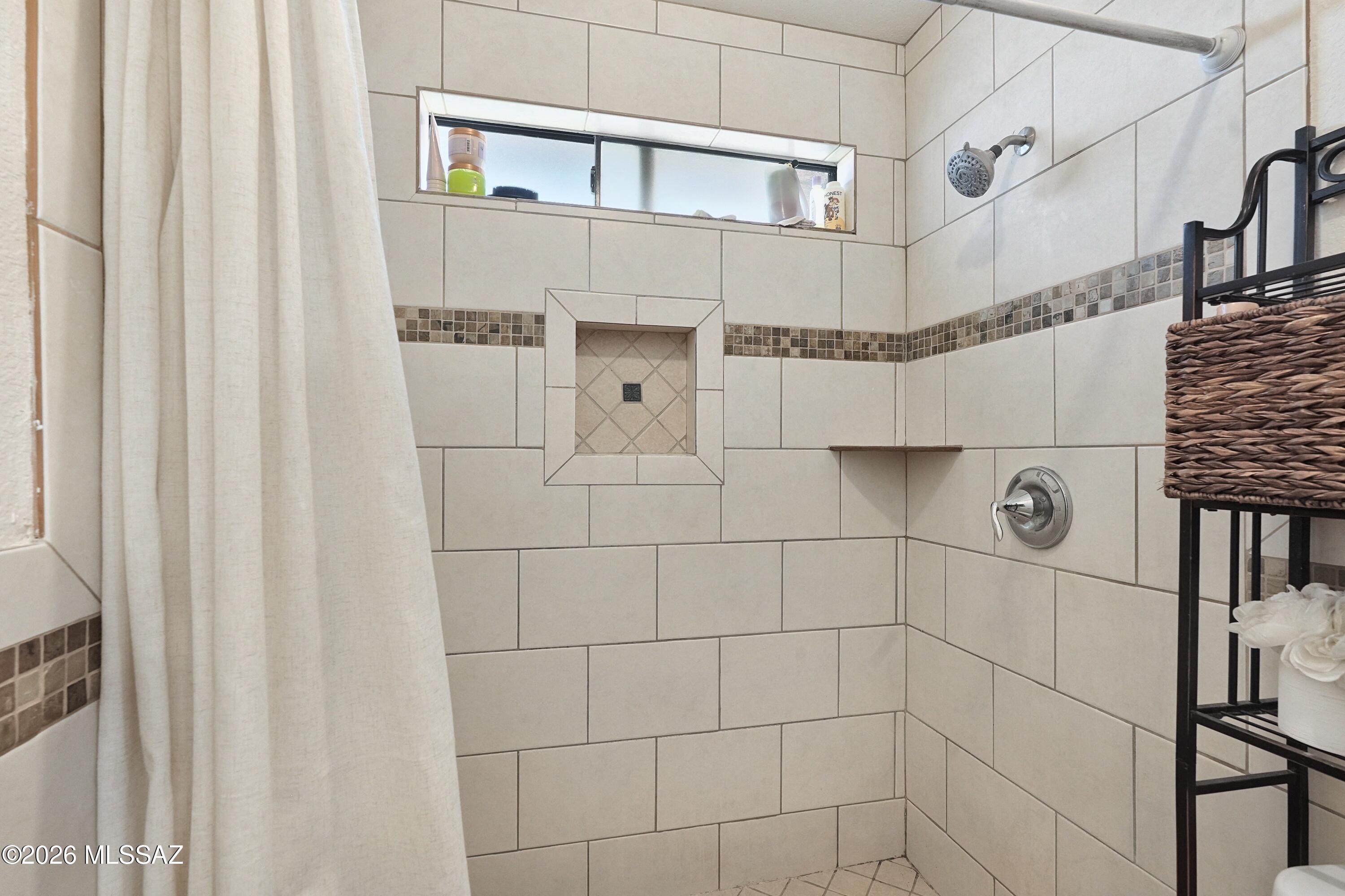 Tiled walk-in shower with a recessed niche, mosaic accent band, and high horizontal window.