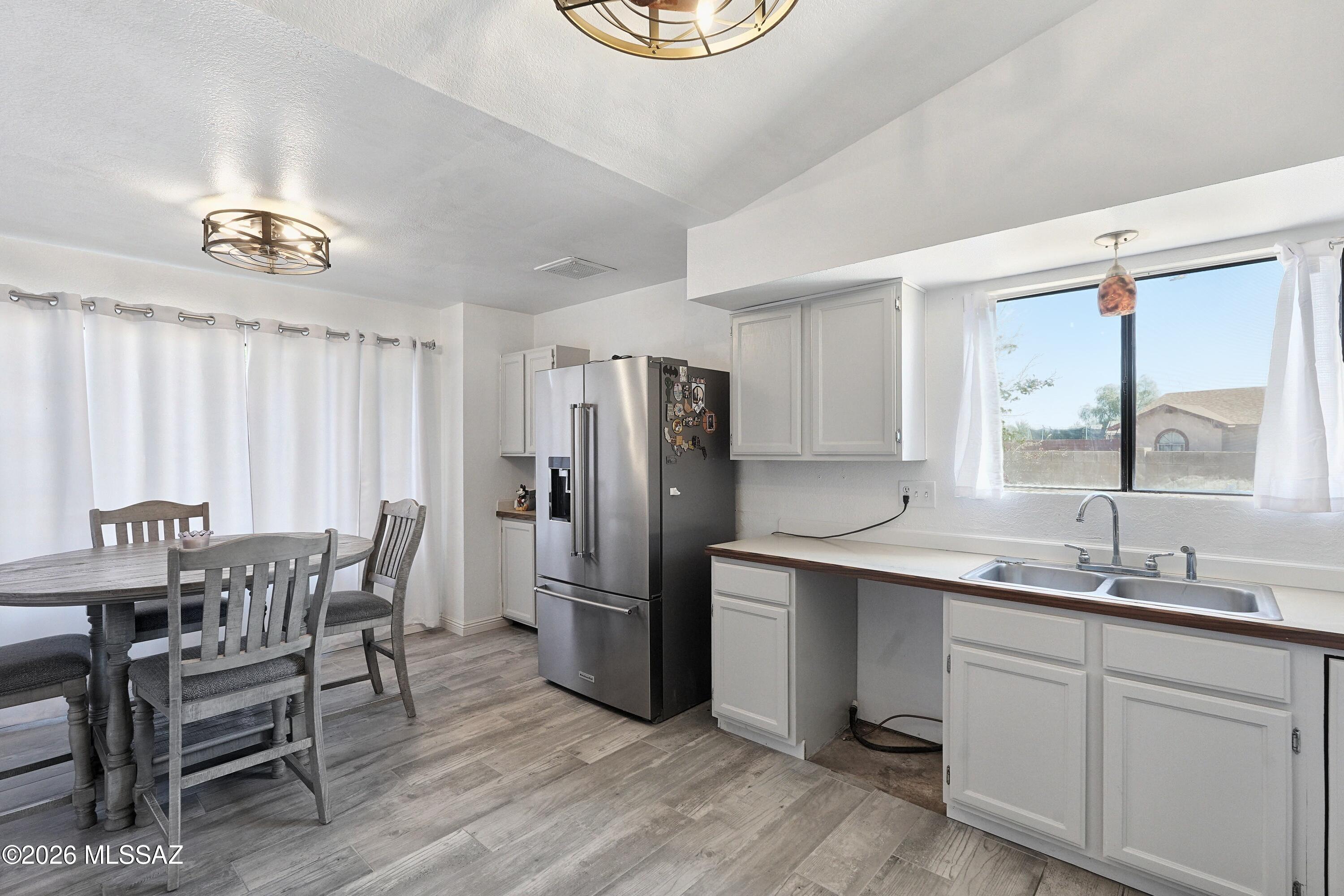 Kitchen and dining area with white cabinets, stainless refrigerator, window-side sink, and round table.