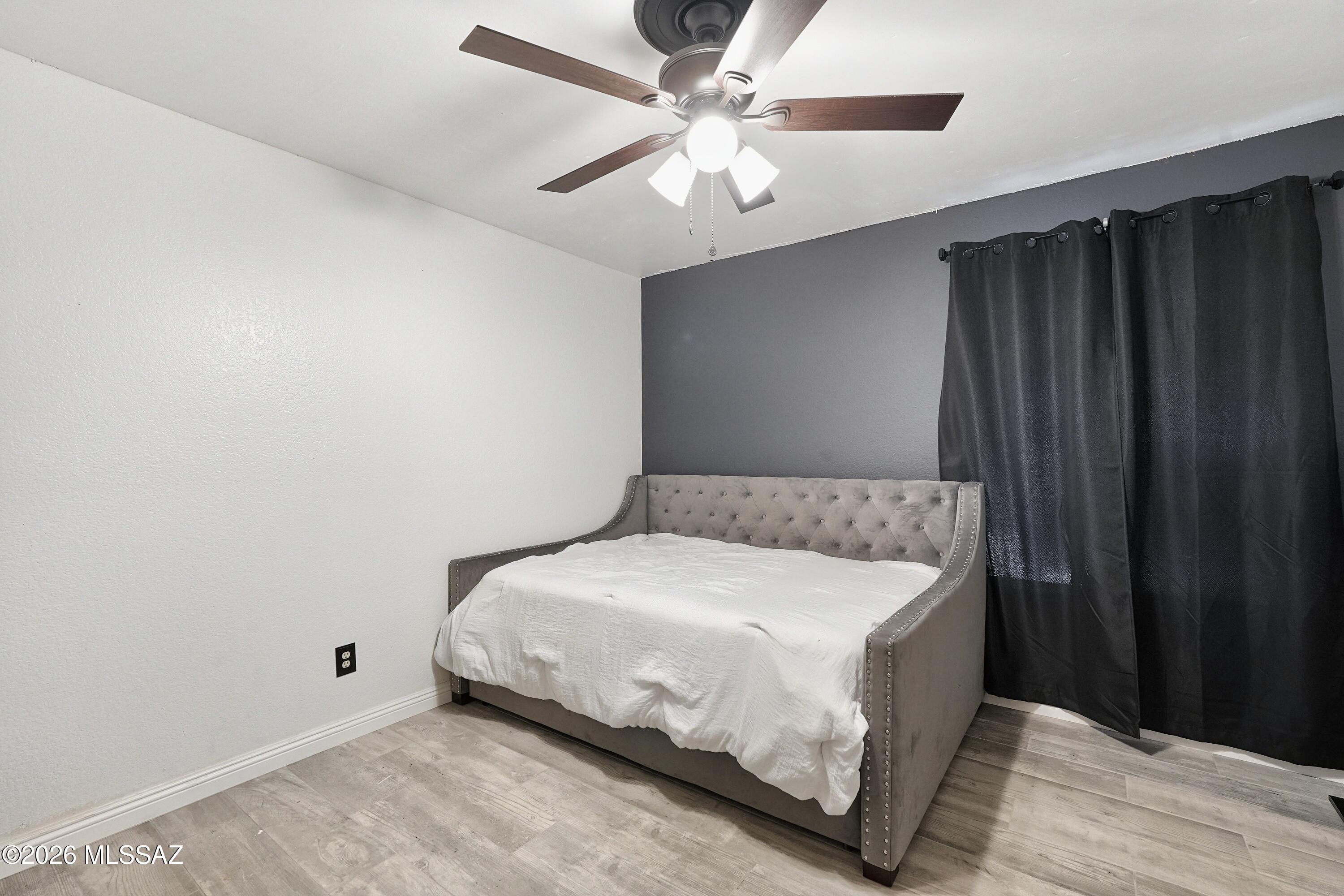Bedroom with a gray upholstered daybed, dark accent wall, black curtains, and ceiling fan.