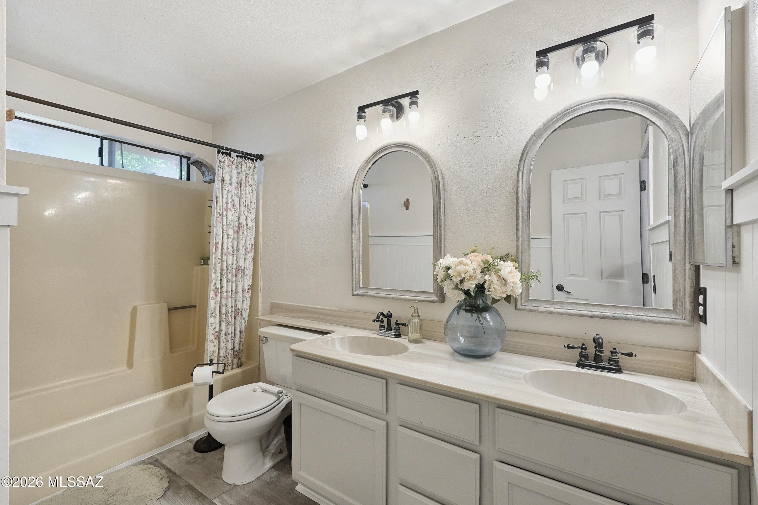 Bathroom with a double-sink vanity, two arched mirrors, and a bathtub with floral shower curtain.