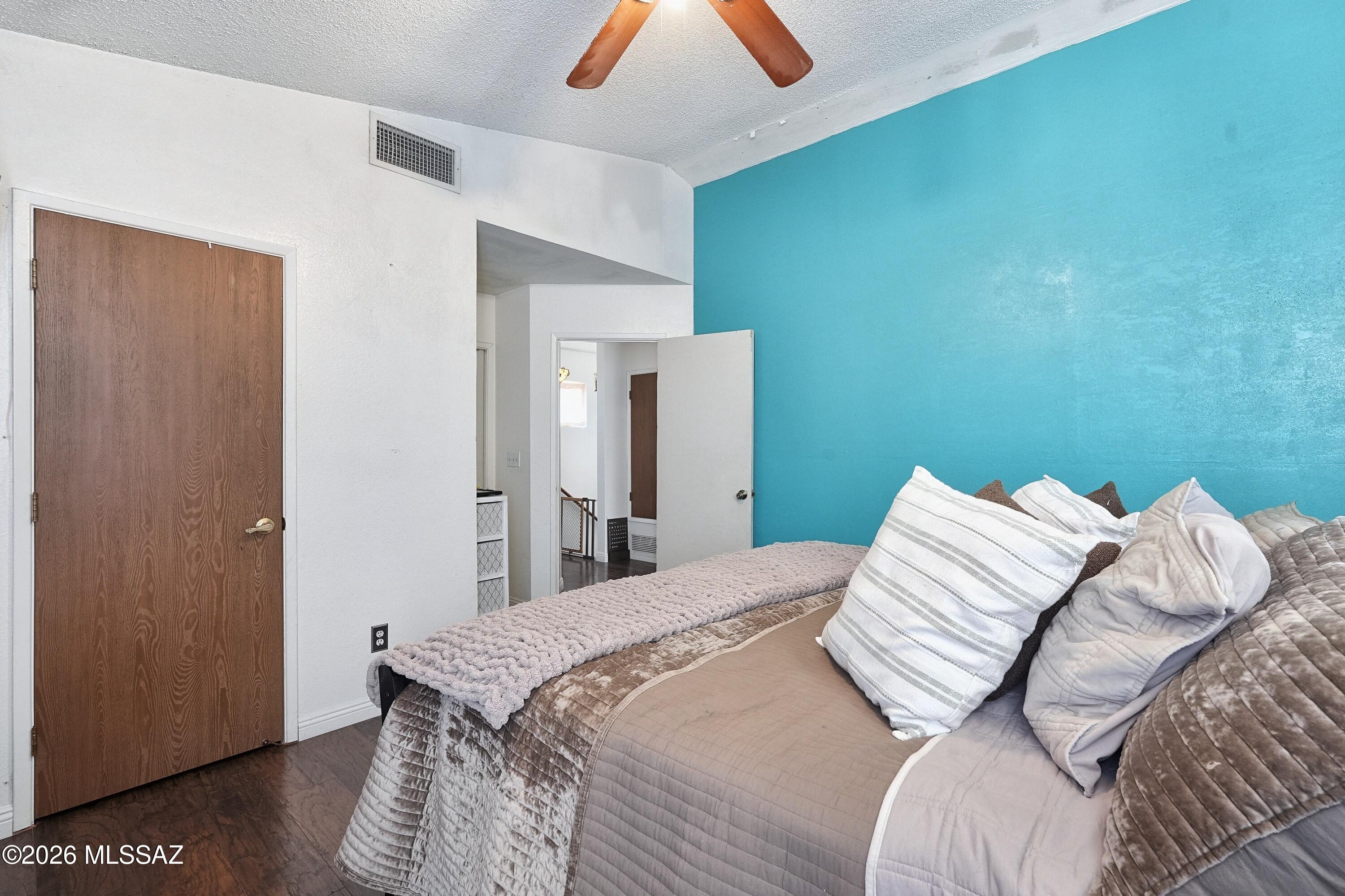 Bedroom with a bed dressed in gray bedding against a vivid turquoise accent wall.