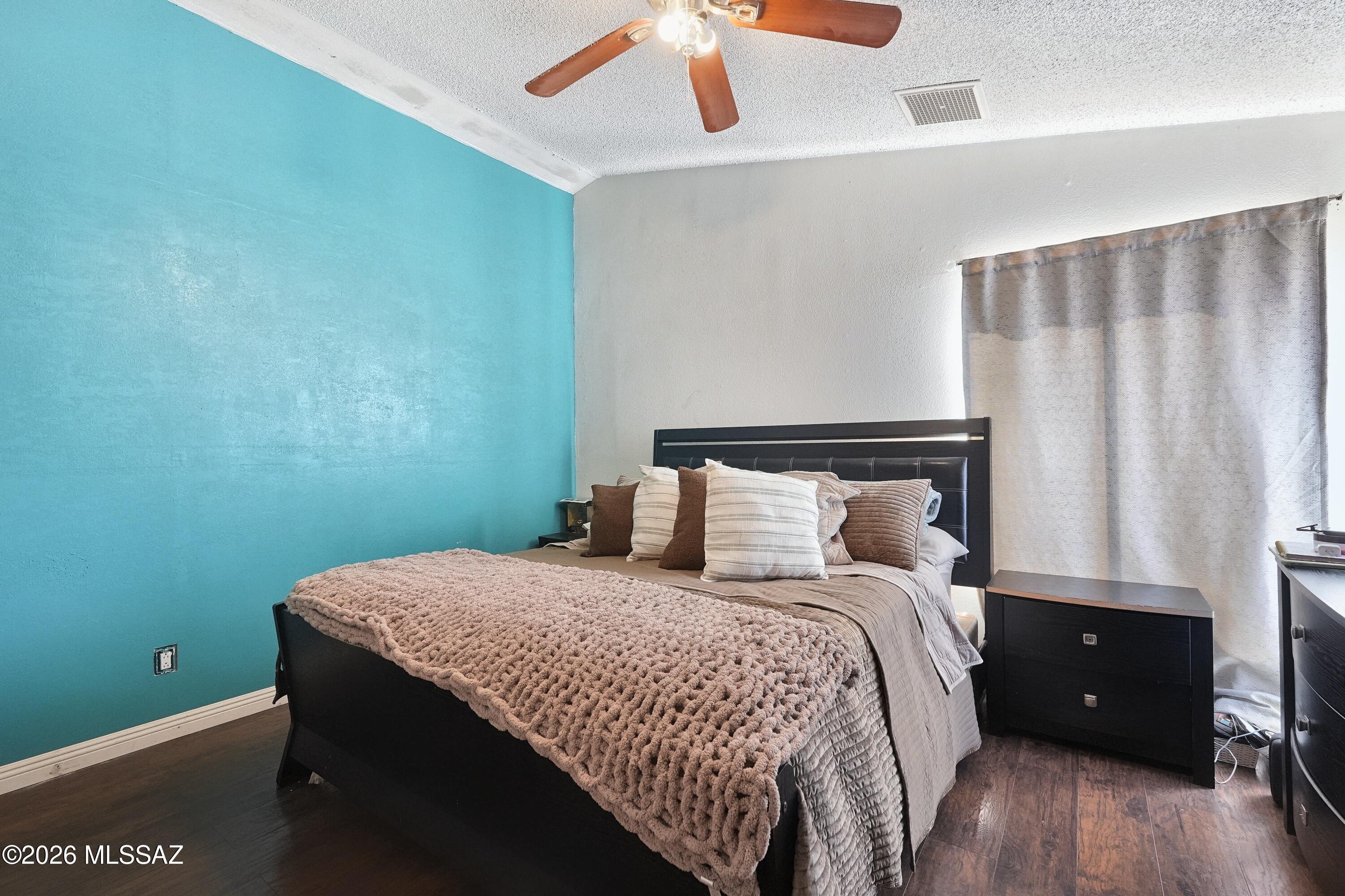 Bedroom with a turquoise accent wall, dark bed, layered neutral bedding, and ceiling fan.