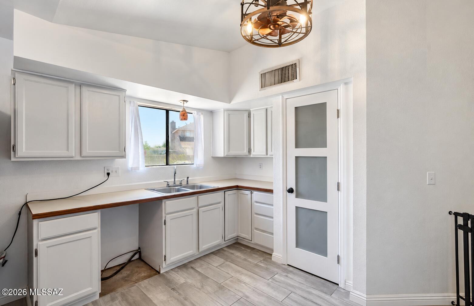 Kitchen with white paneled cabinets, wood-trimmed counters, and a sink beneath a window.