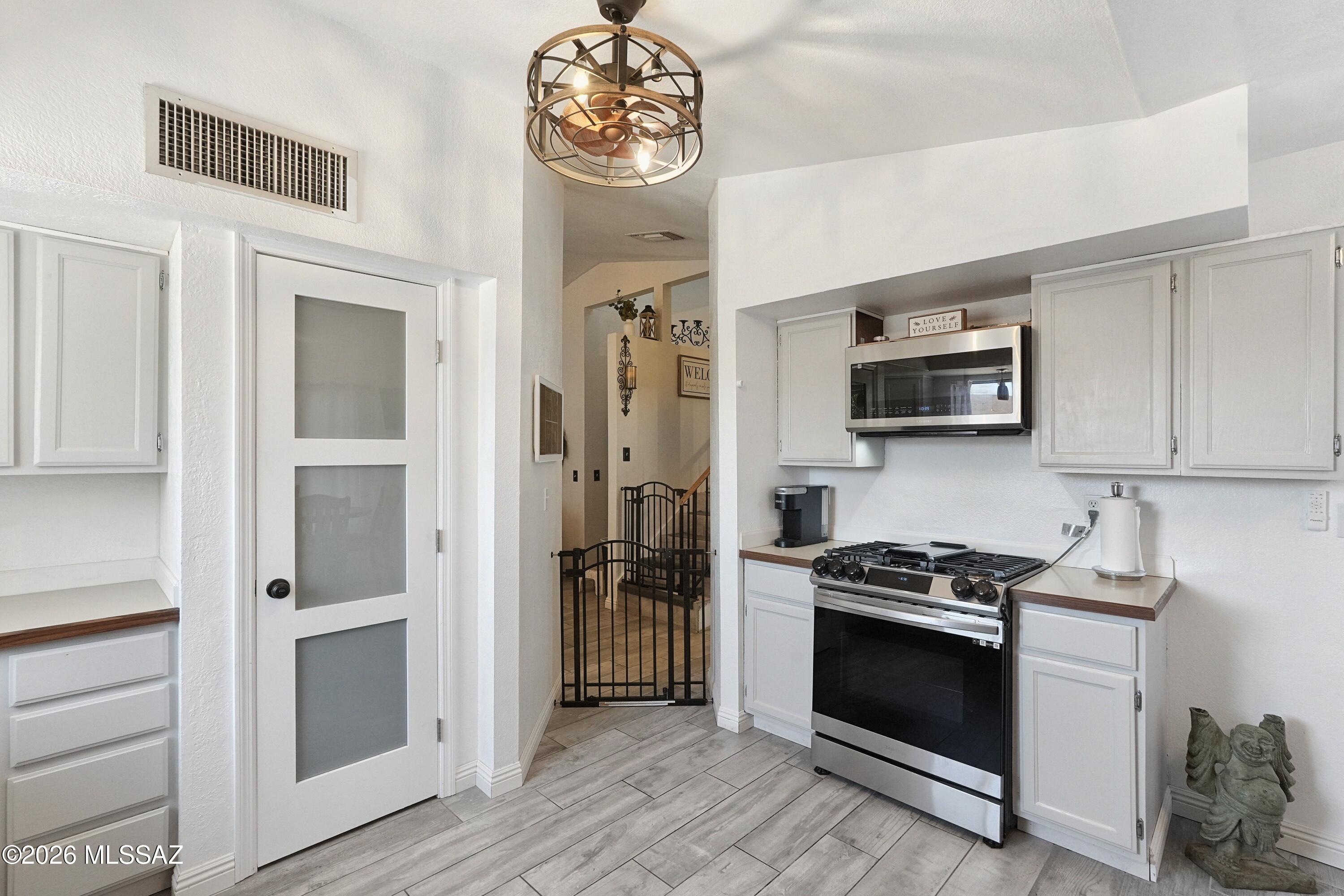 Kitchen with white cabinets, stainless steel range and microwave, and a gated opening to the hall.