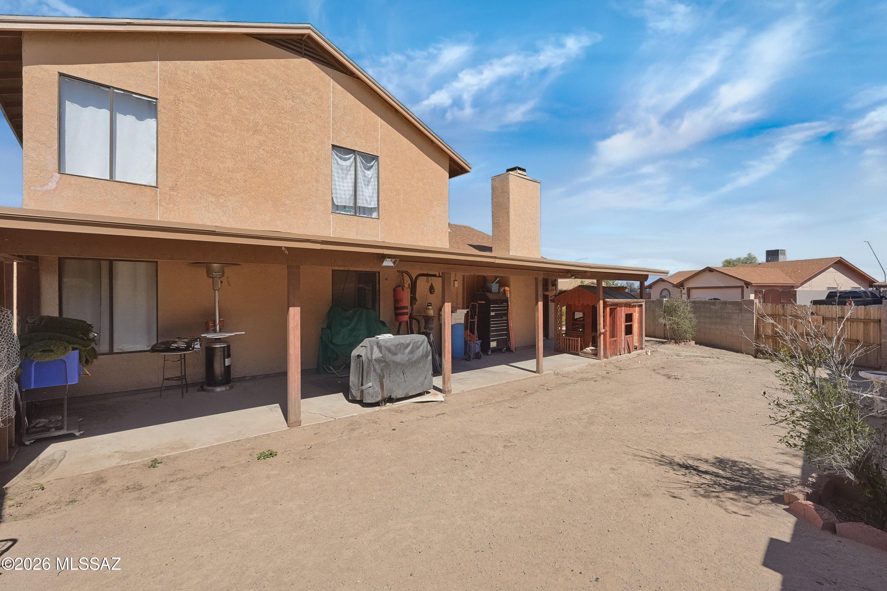 Two-story stucco home with a covered rear patio and bare dirt backyard.