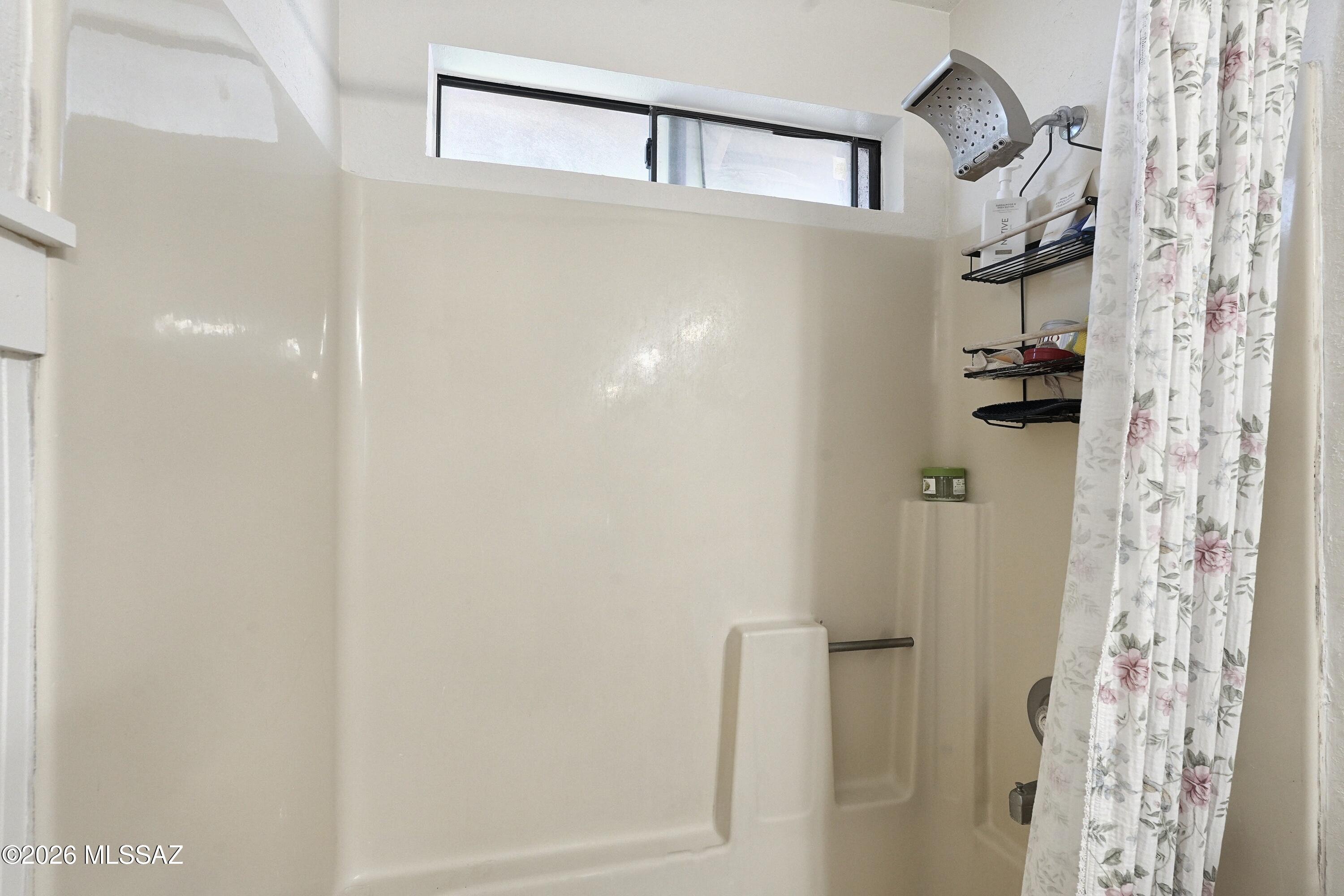Bathroom tub and shower with high window, wall-mounted shelves, and floral shower curtain.