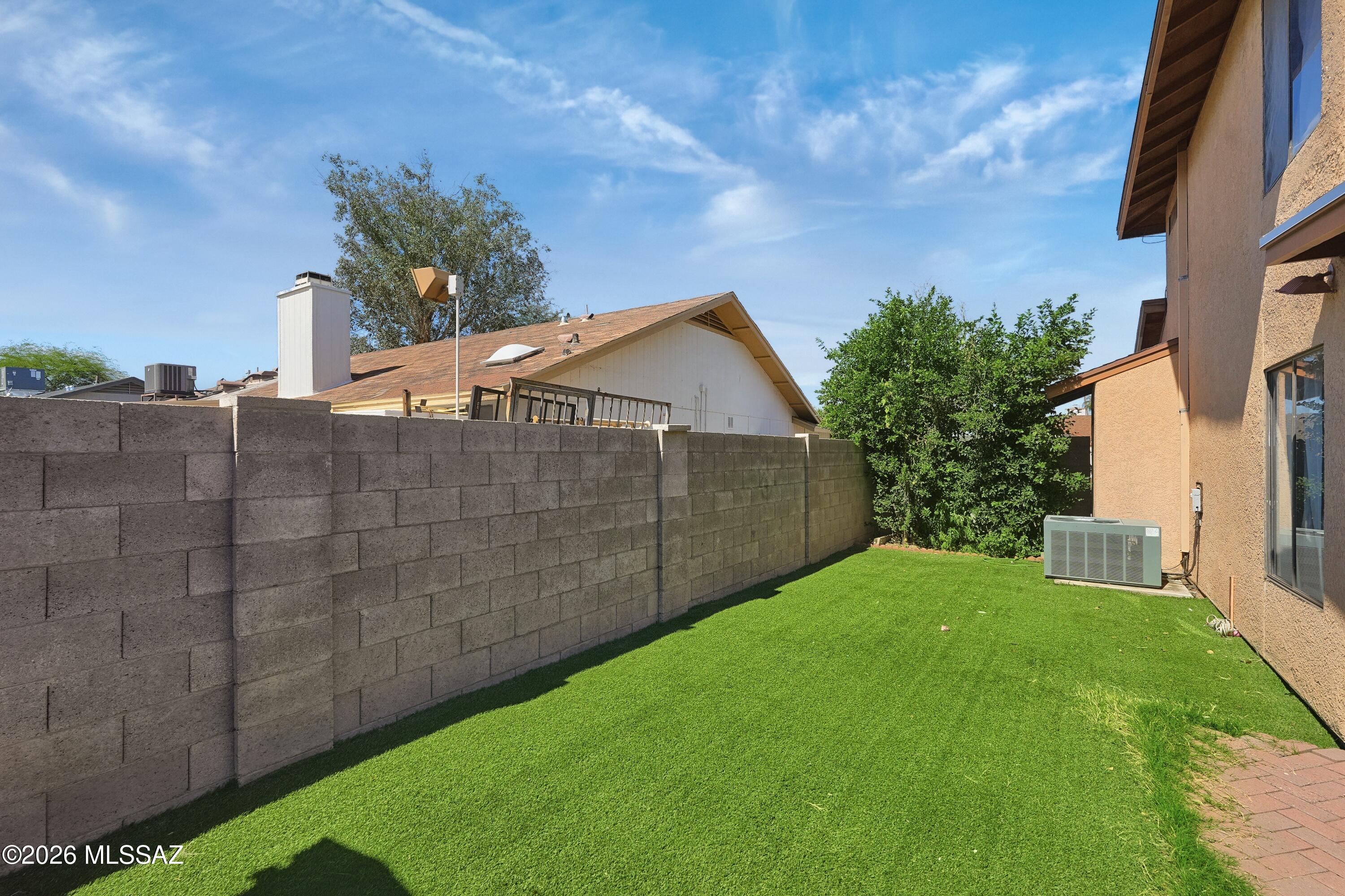Side yard with green lawn, tall block wall, shrubs, and the stucco house exterior.