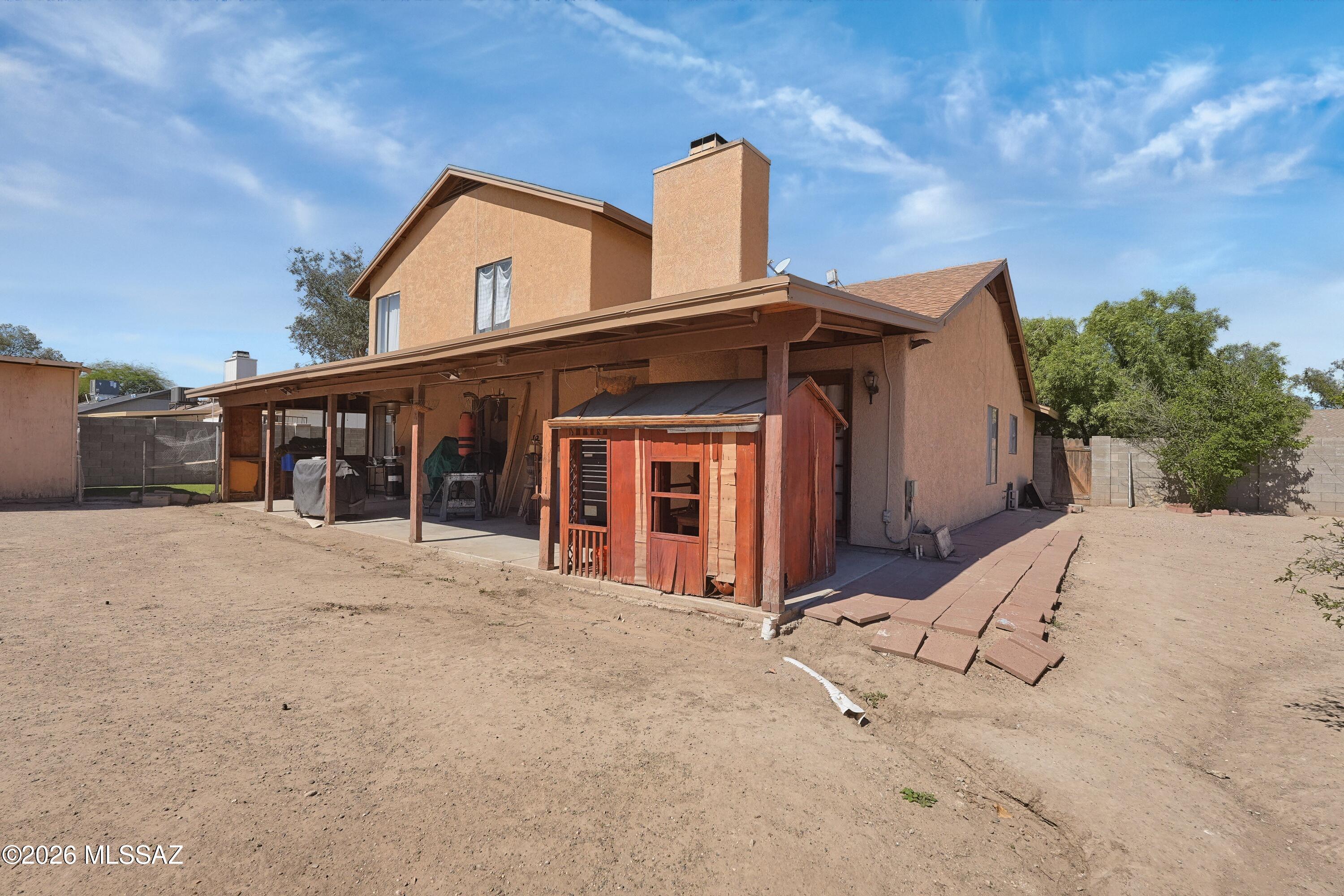 Two-story stucco home with a covered rear patio, wooden shed, and bare dirt yard.