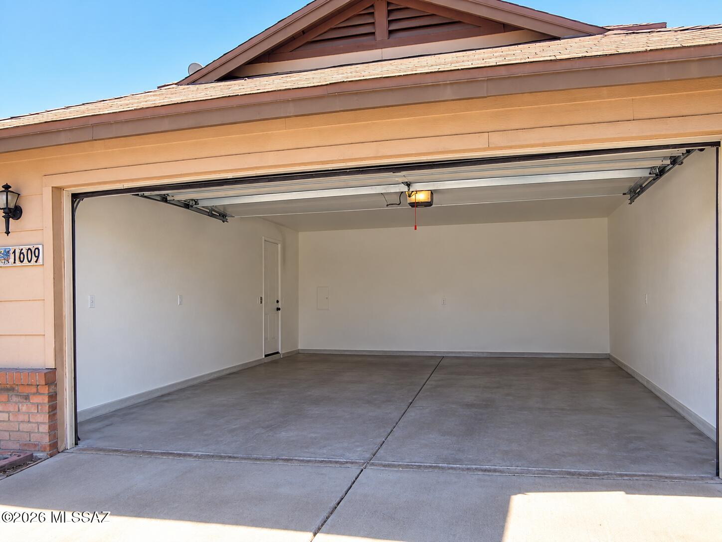 Open empty garage with a concrete floor, white walls, and tan exterior.