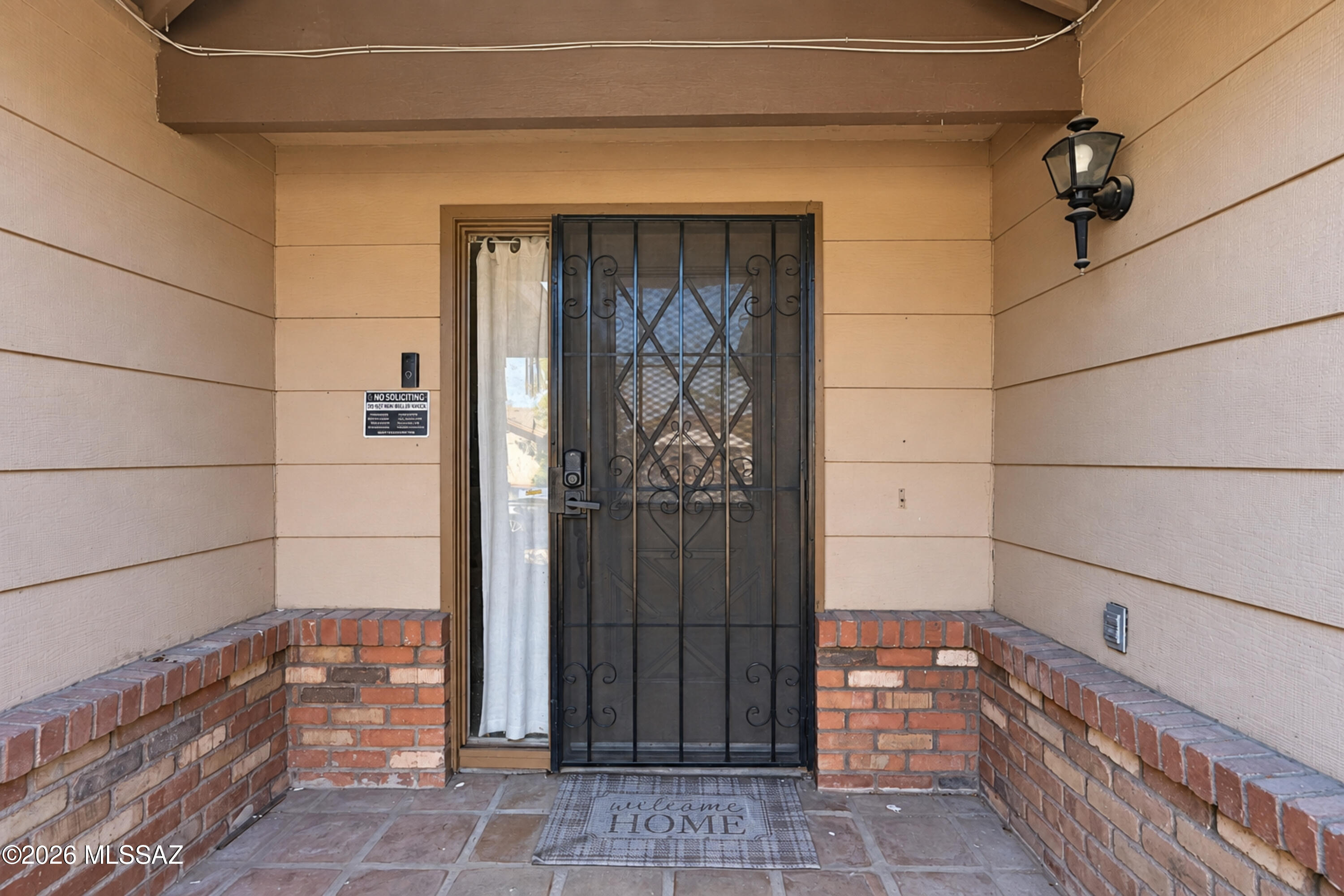 Covered home entry with a black decorative security door, brick porch walls, and a welcome mat.