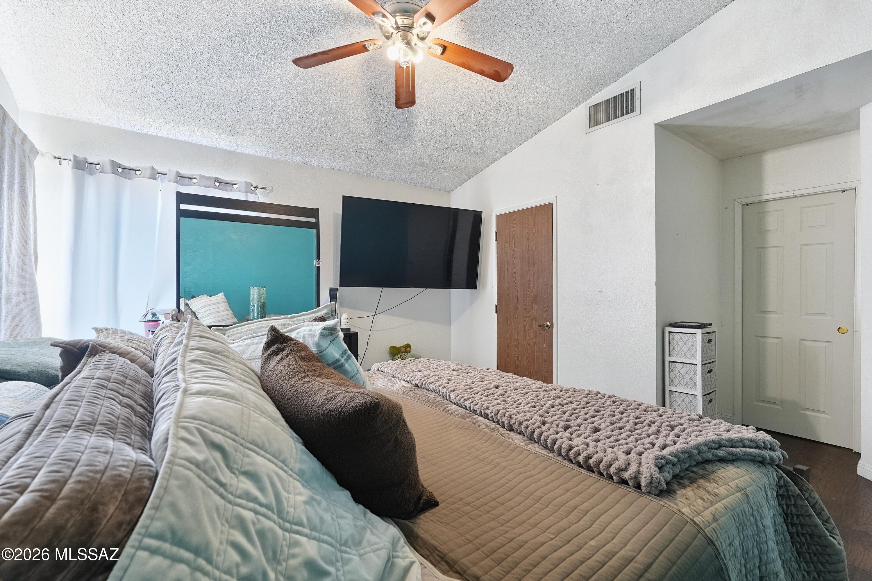 Furnished bedroom with layered gray and teal bedding, a turquoise headboard, and a wall-mounted television.