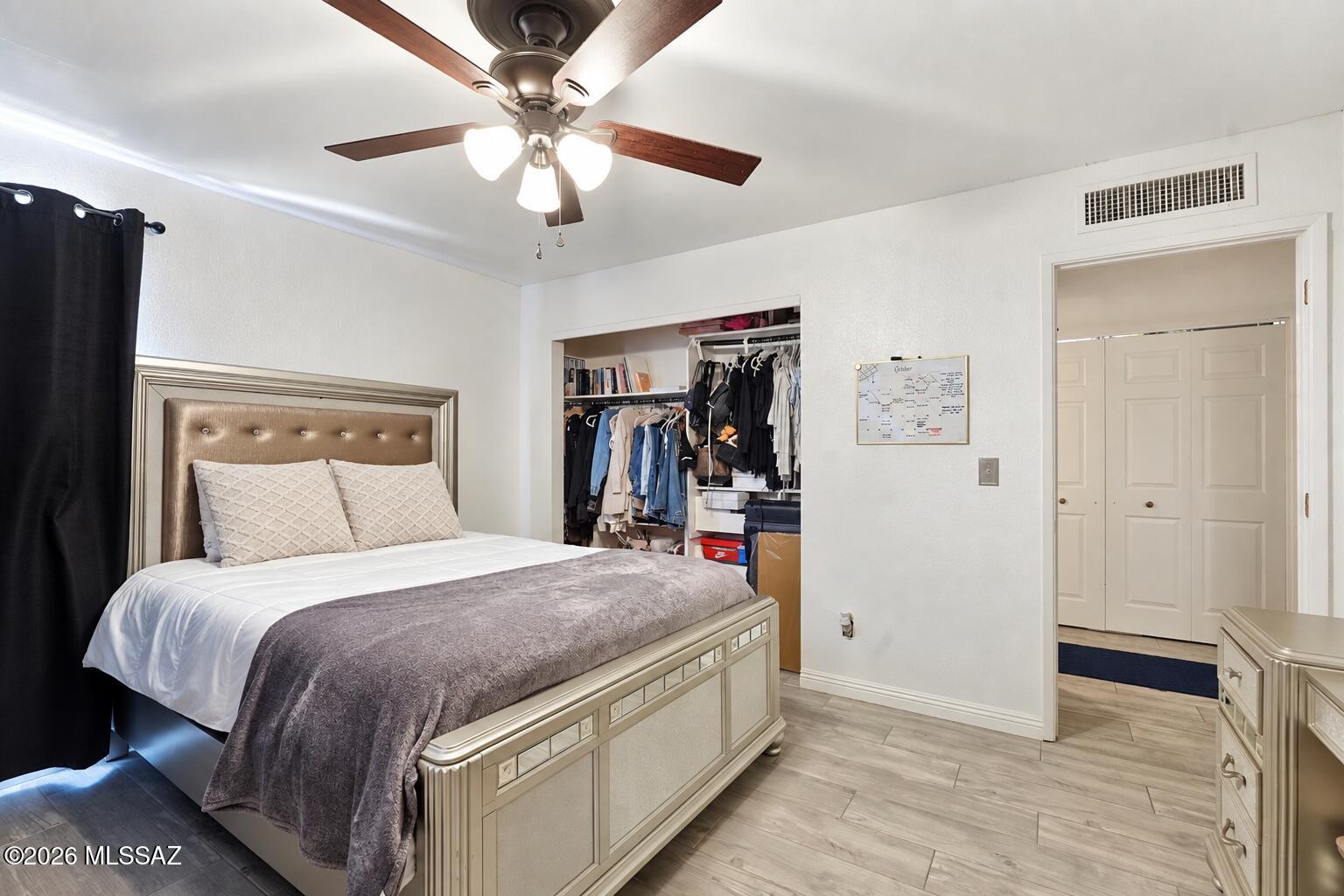 Furnished bedroom with a large bed, open clothes closet, black curtains, and a ceiling fan with lights.