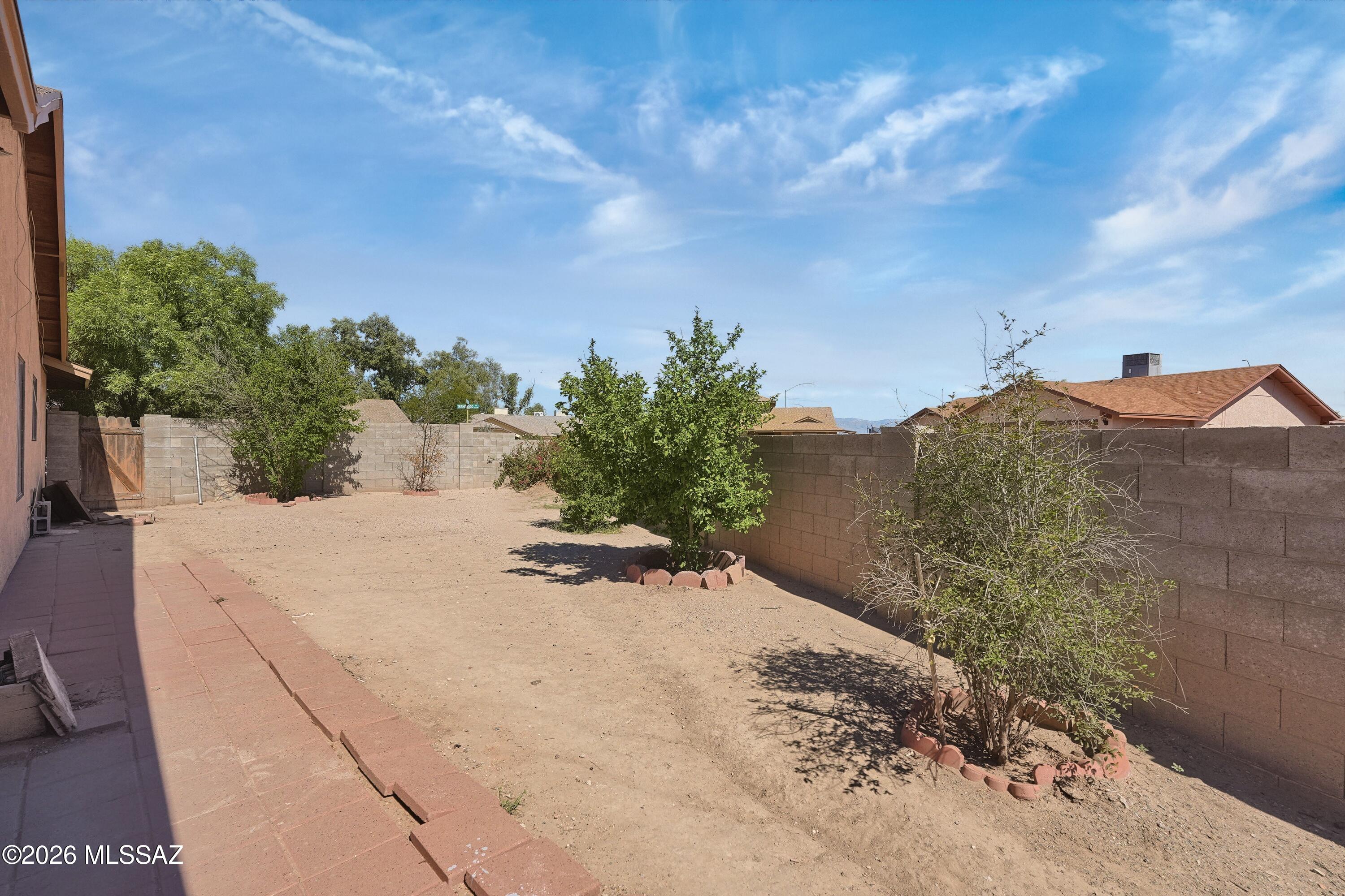 Enclosed backyard with a sandy yard, scattered shrubs, block walls, and a paved walkway beside the house.