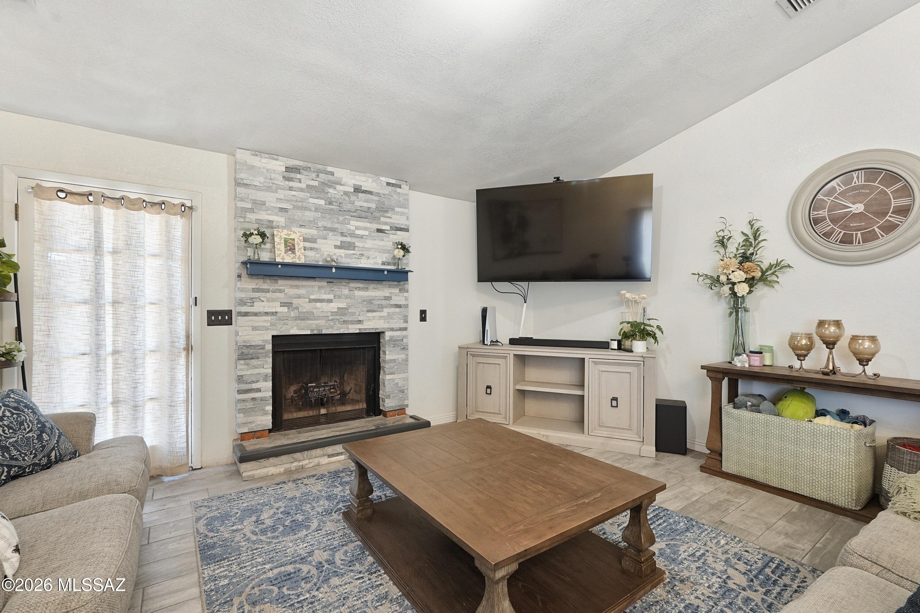 Living room with a gray stone fireplace, wall-mounted television, and large wooden coffee table.