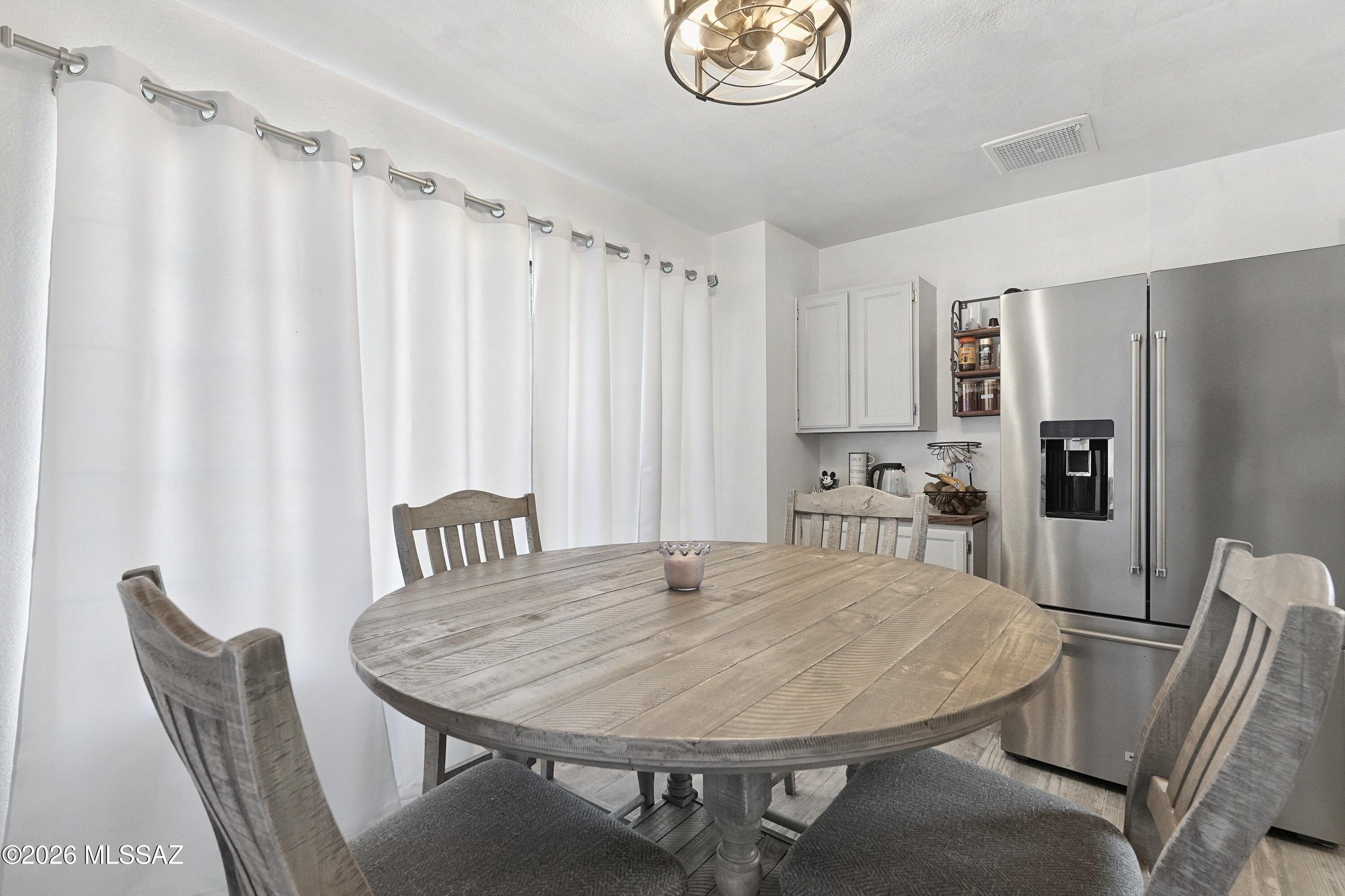 Dining area with a round gray wood table, matching chairs, and a stainless steel refrigerator.