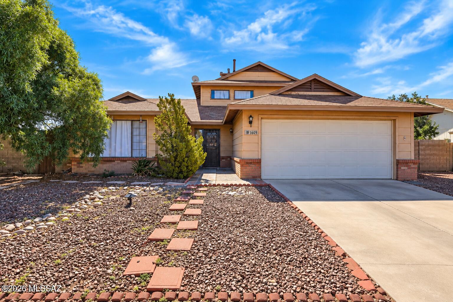 Tan two-story Tucson home with a broad garage and desert gravel landscaping with stepping stones.