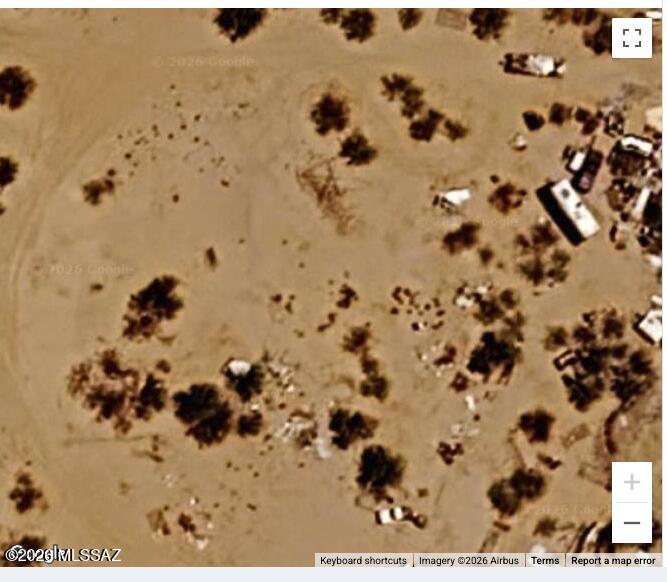 Aerial view of open desert land with scattered trees and a few nearby structures.
