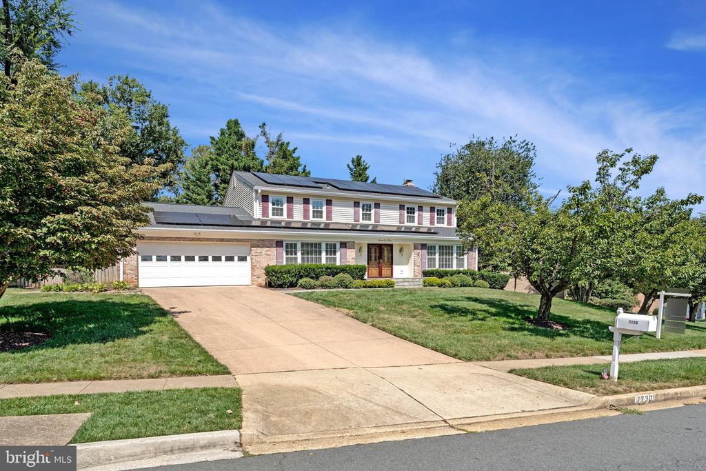 Two-story house with solar panels, brick accents, attached garage, and a wide driveway.