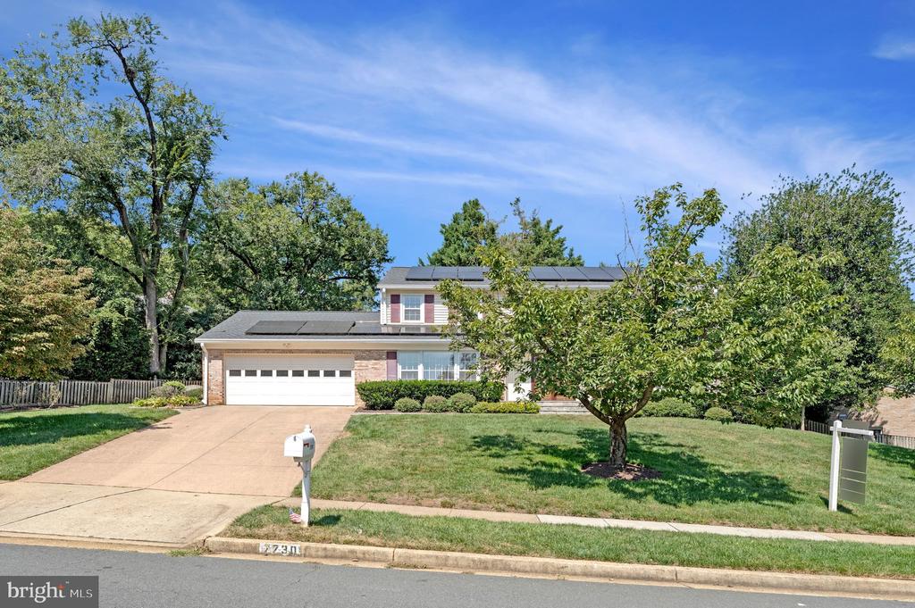 Two-story home with rooftop solar panels, an attached garage, and a tree-shaded front lawn.