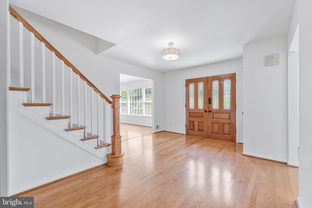 Entry foyer with hardwood floors, a glass-paneled wooden front door, and a staircase with wood handrails.
