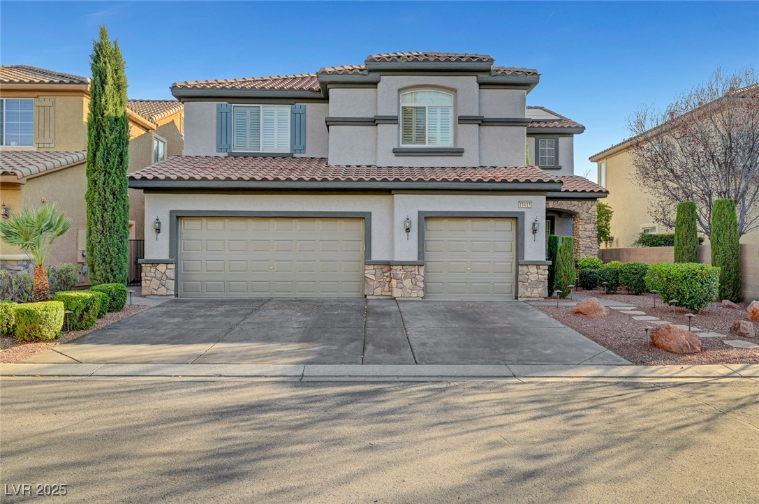 Two-story stucco house with stone accents, two garage doors, and desert landscaping.