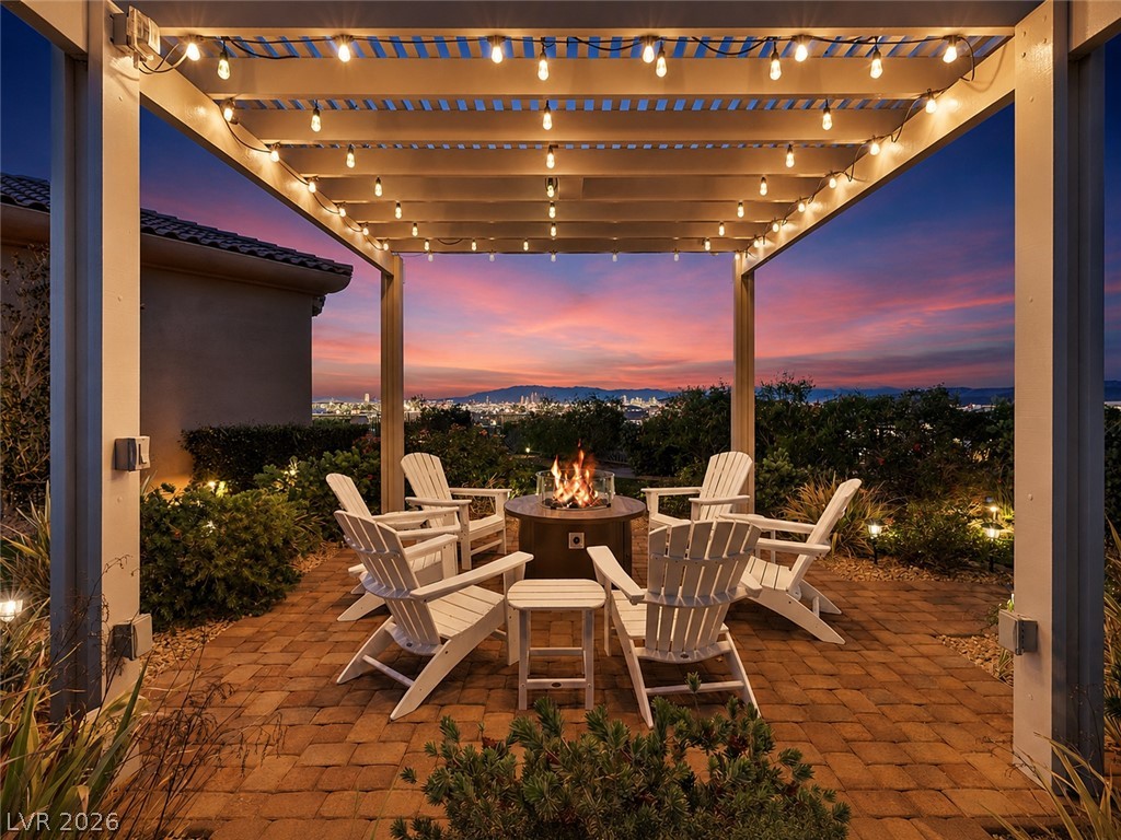 Patio with a lit pergola, fire pit, Adirondack chairs, and city skyline at sunset.