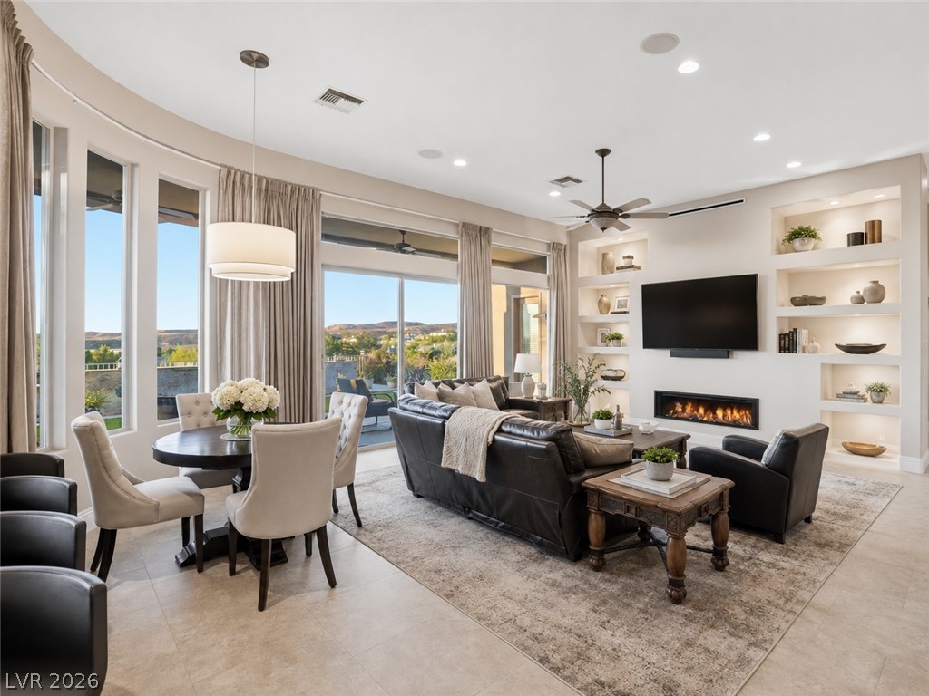 Open-plan living and dining room with curved windows, leather seating, built-in shelves, and a linear fireplace.