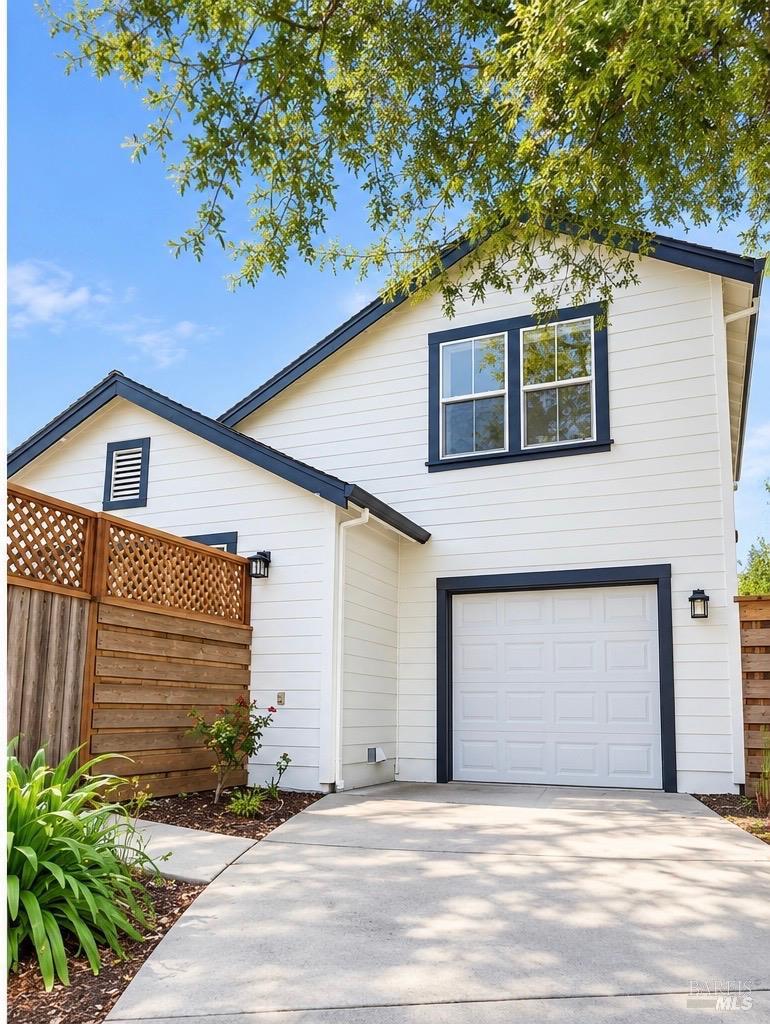 White two-story home with dark trim, a garage, and a wooden privacy fence.