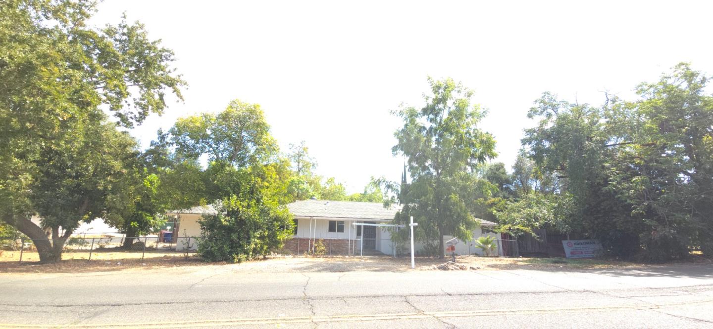 Single-story home partly screened by mature trees, viewed from across the street.