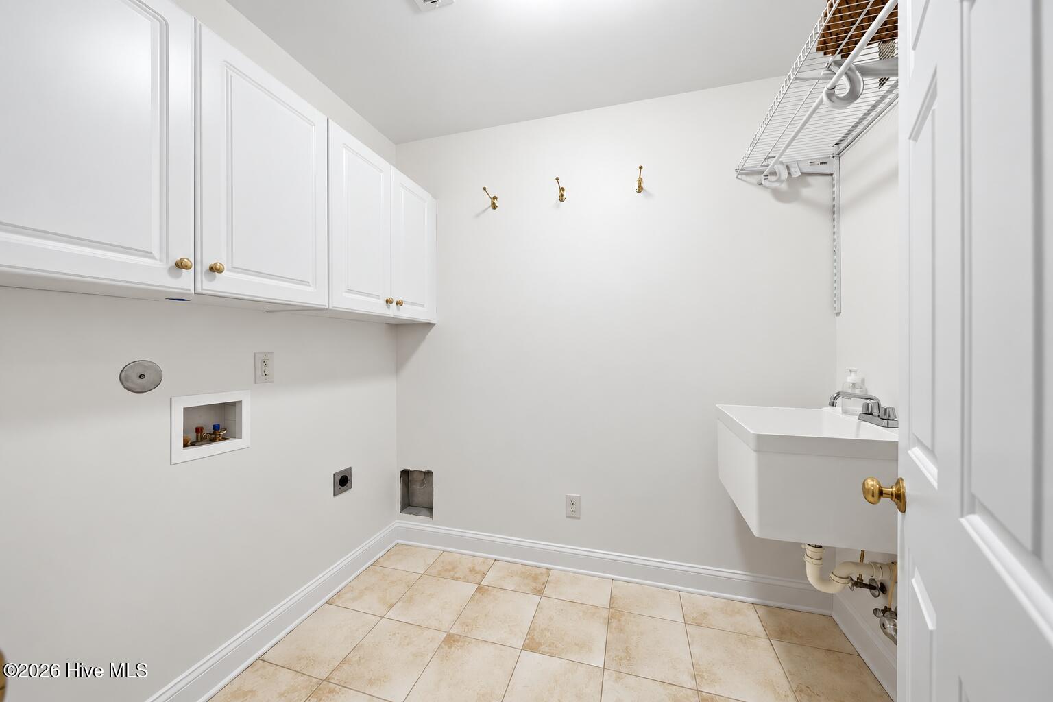 Laundry room with white cabinets, washer and dryer hookups, utility sink, and beige tile floor.