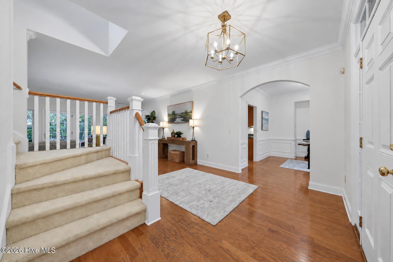 Entry foyer with carpeted staircase, white railings, hardwood floors, and a brass chandelier.