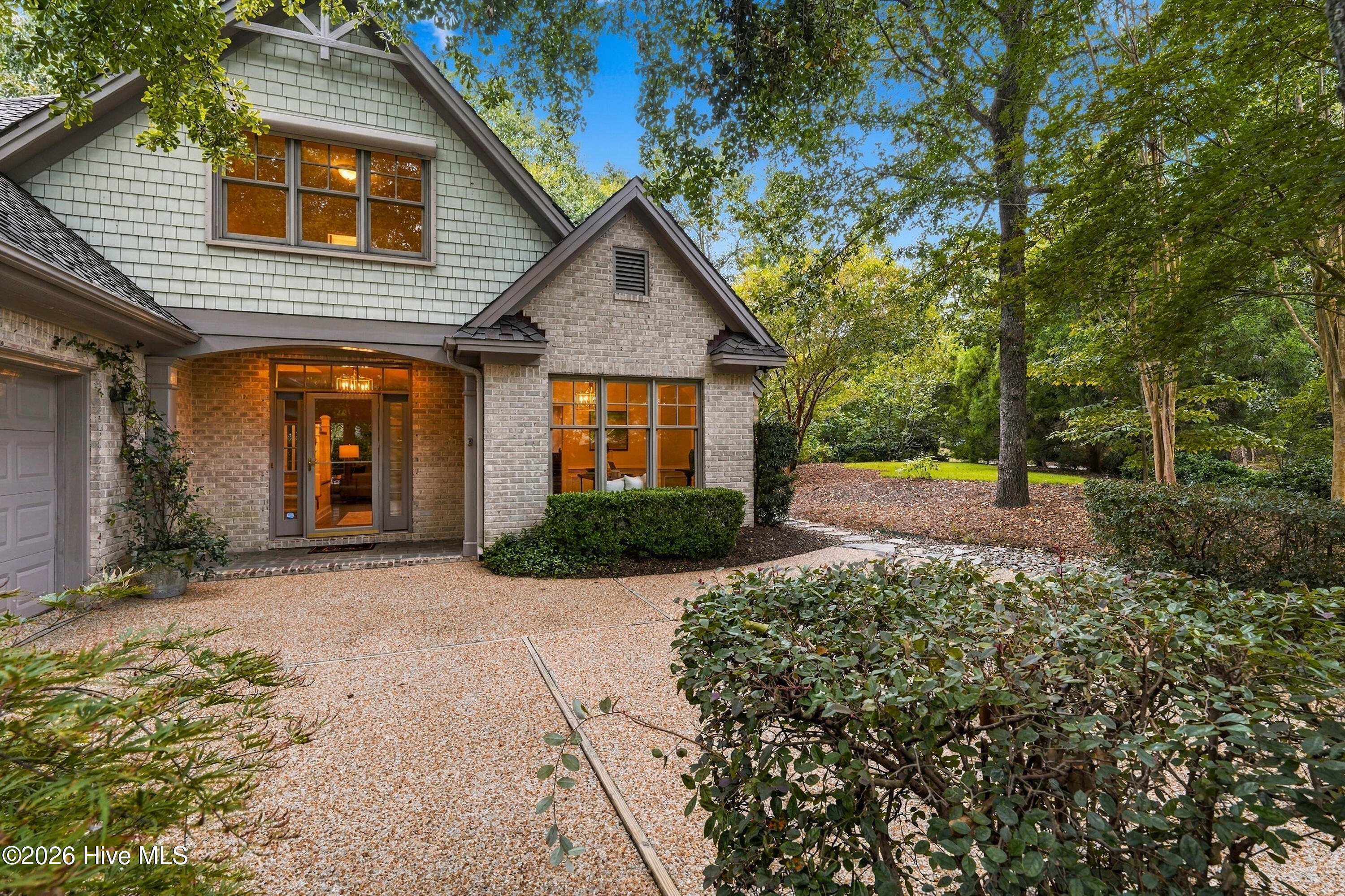 Two-story brick and shingle home with a broad gabled facade and a tree-lined landscaped walkway.