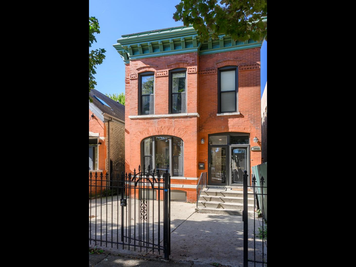 Red-brick townhouse with an ornate green cornice behind a black iron gate.