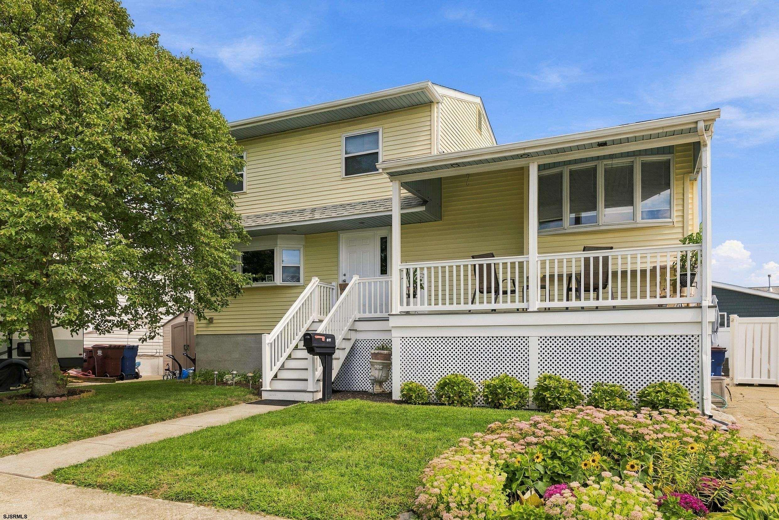 Pale yellow two-story home with a covered porch, white railings, and a flower garden.