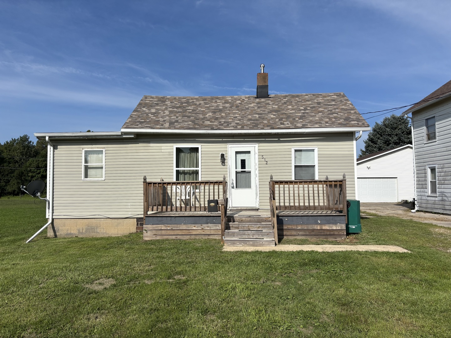Single-story beige house with a raised wooden porch, front steps, and green lawn.