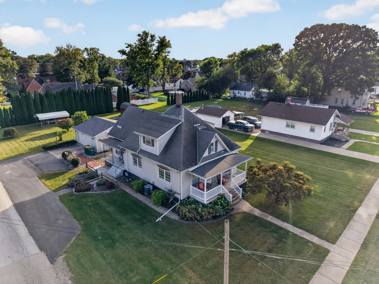 Aerial view of a two-story home with a gray roof, white porch, landscaped garden, and broad lawn.