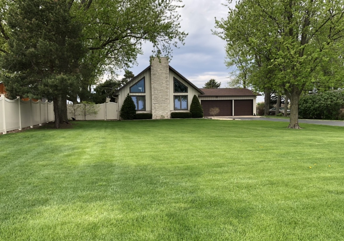 Gabled house with a tall stone chimney, attached two-car garage, and broad green lawn.